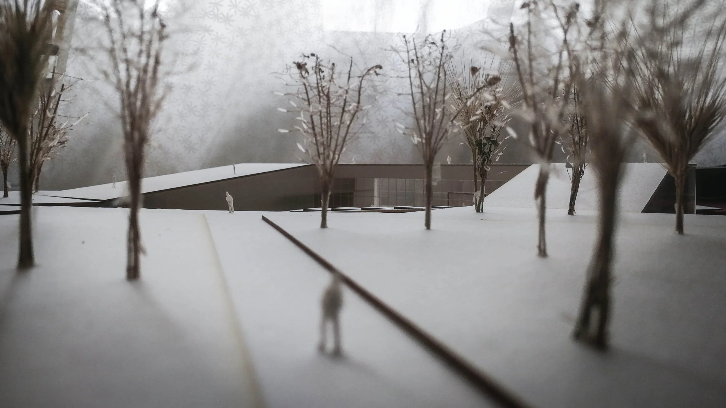 A model of a modern building surrounded by leafless trees and snow, with a misty background.