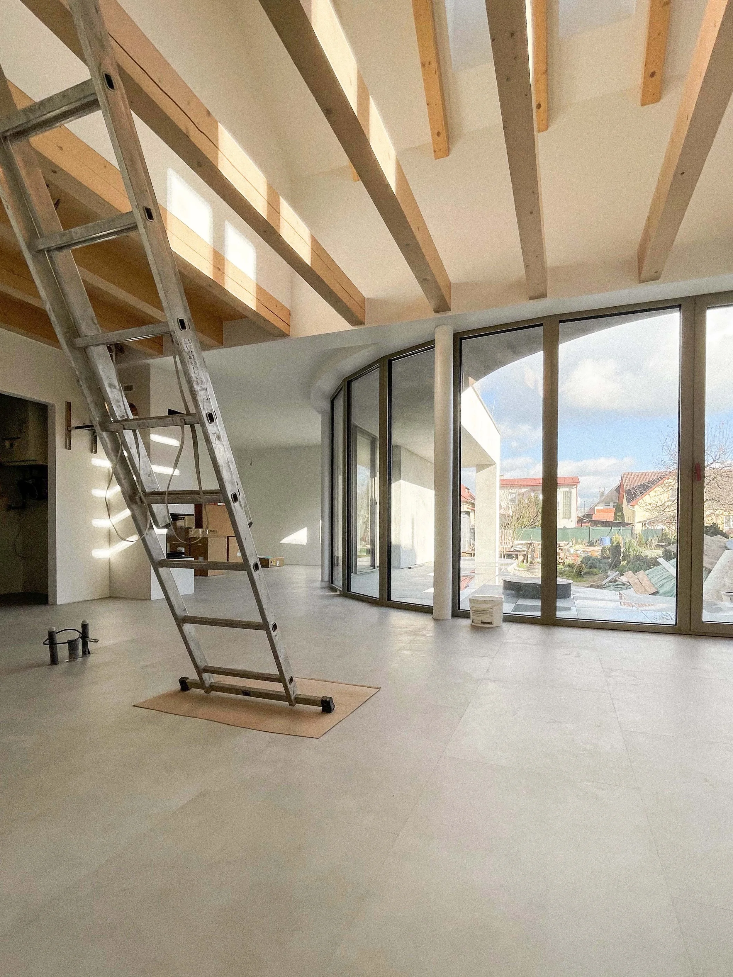 An unfinished interior space with an arched ceiling, large glass window doors, and a ladder leaning against the wall. The space appears to be under construction or renovation with tools and materials present.