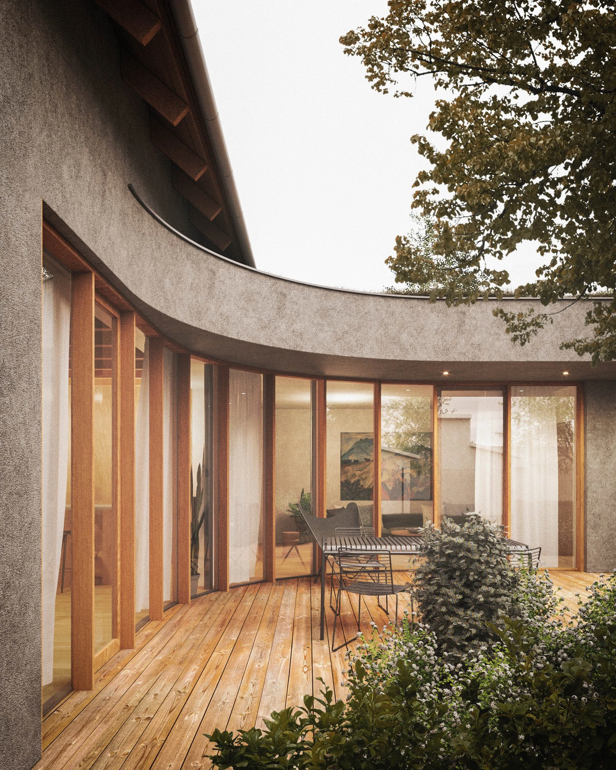 View of a modern house with a curved exterior wall and large glass windows, surrounded by trees and a wooden deck with outdoor furniture.