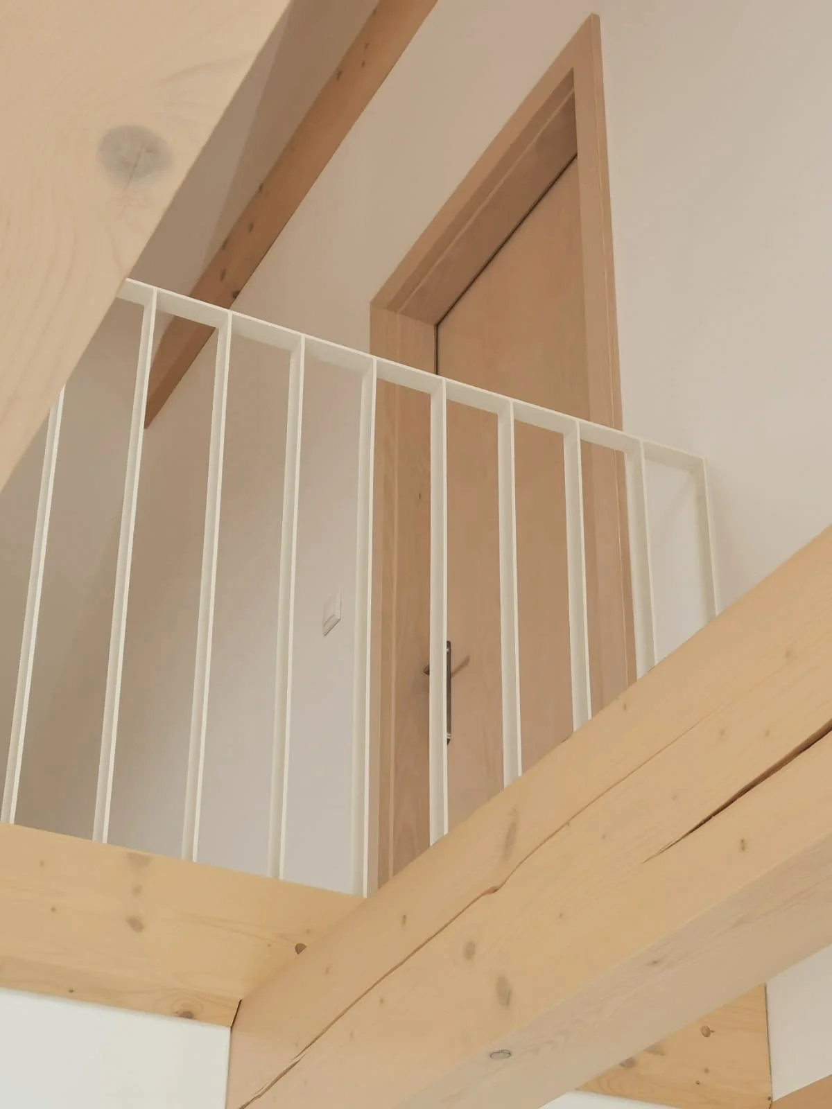 Interior view of a wooden staircase with a safety railing, looking up at a door on the upper level.