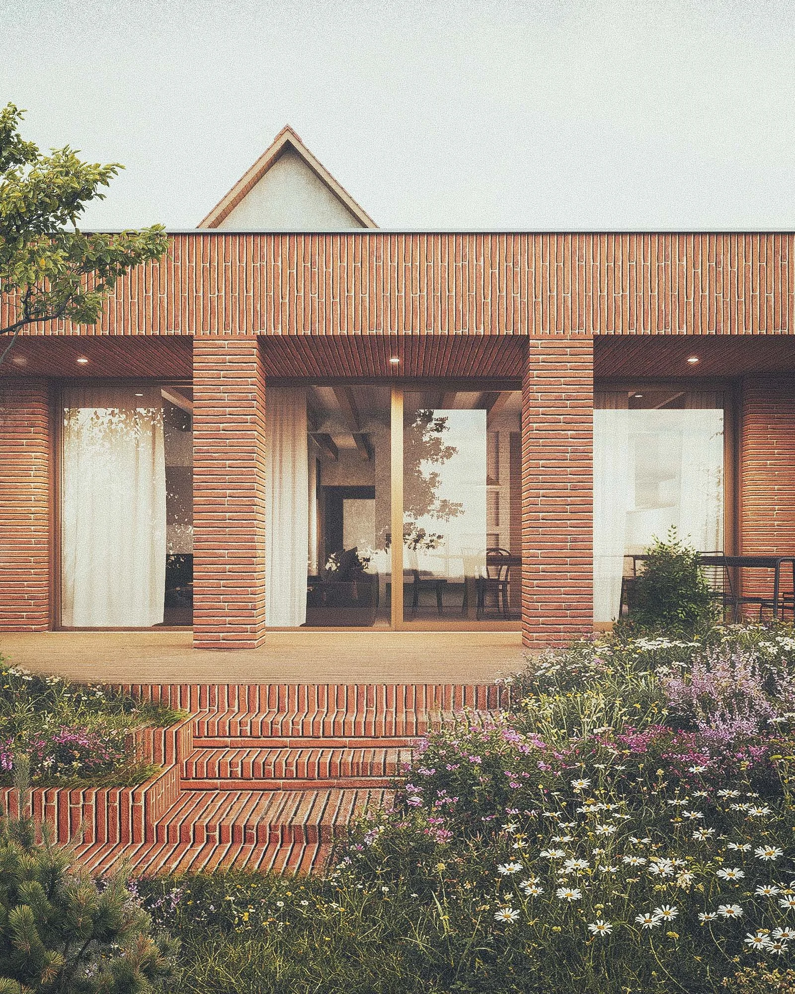 A modern brick house with large windows, a balcony, and an outdoor patio, surrounded by blooming flowers and greenery.