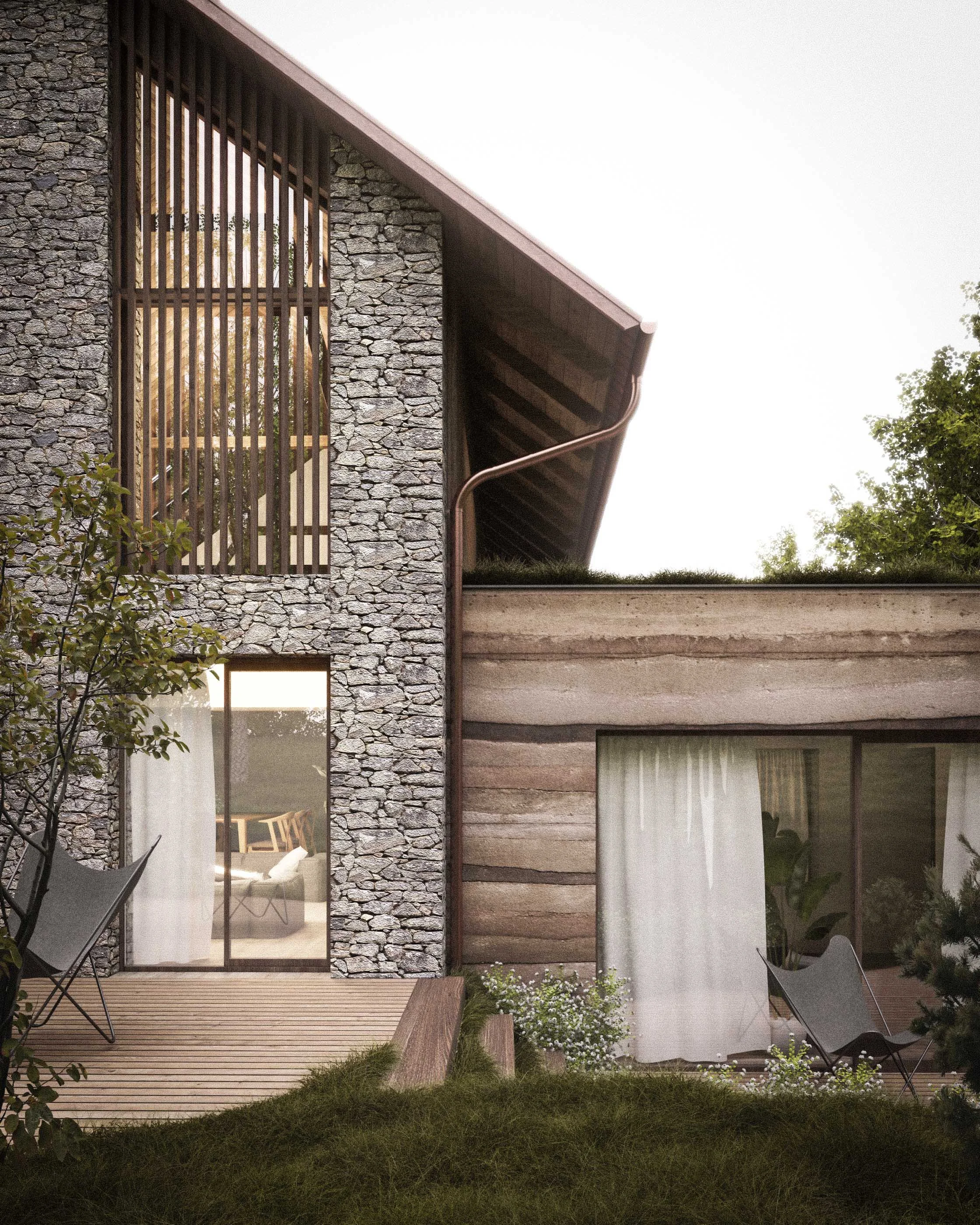 Exterior view of a modern house with a stone facade, large glass doors leading to a wooden deck, and a partially visible garden with green grass and small white flowers. Two black chairs are on the deck.