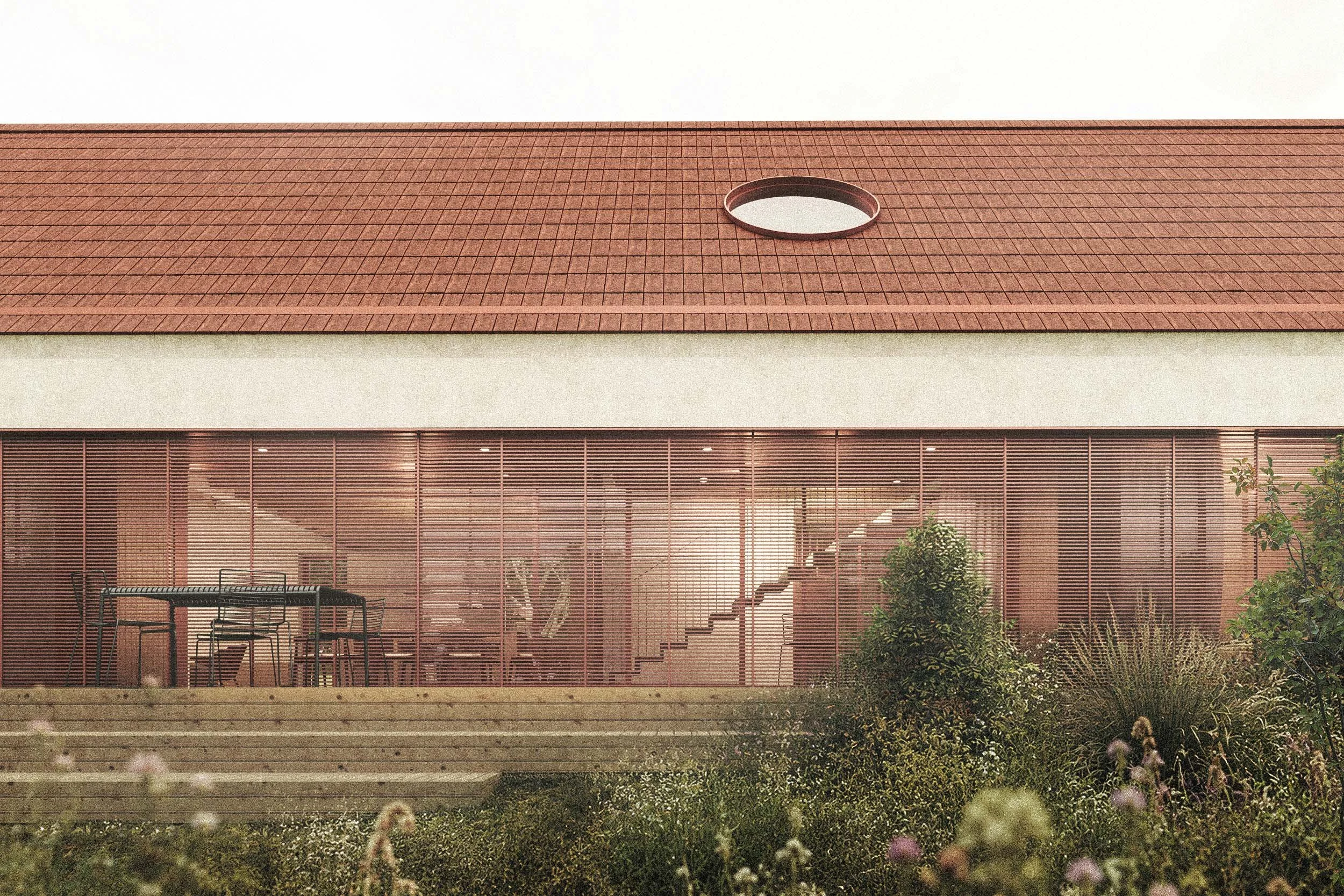 Modern building with large glass windows, a red tiled roof with a circular vent, and a small outdoor seating area with chairs and tables, surrounded by greenery.