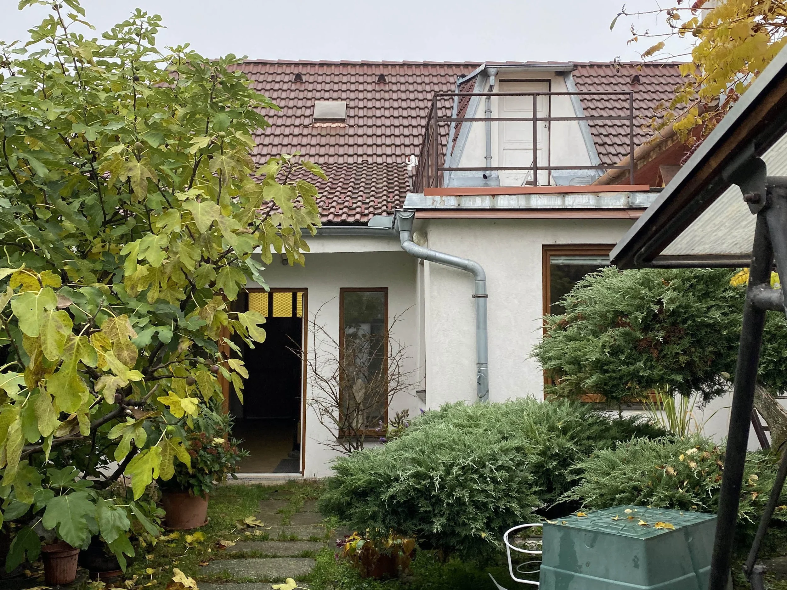 View of a house with a red tiled roof, surrounded by trees and greenery in a garden.