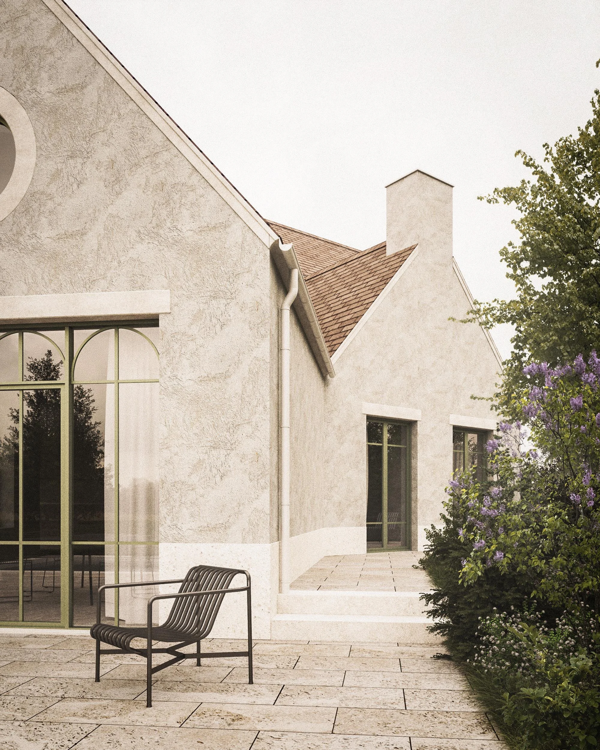 Exterior of a house with cream-colored stucco walls, a large arched window with divided panes, and a small patio with a metal bench. There are trees with purple flowers and a tiled walkway.