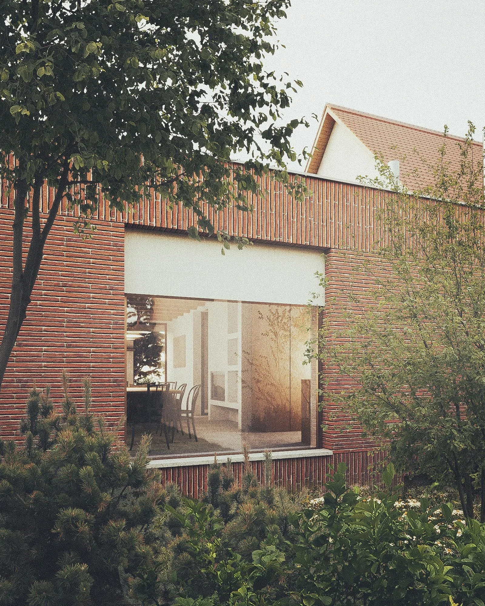 A house with a brick exterior, large window, and a sloped roof, surrounded by trees and greenery.