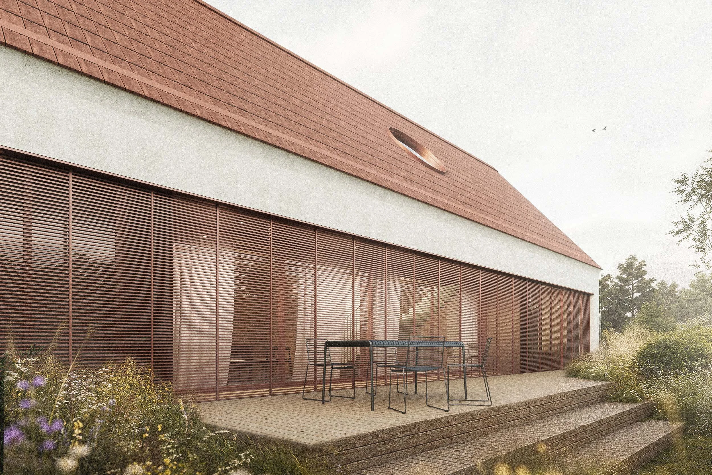 Modern building with a sloped red roof, horizontal wooden slats on the exterior, and a small patio with chairs and a table, surrounded by greenery.