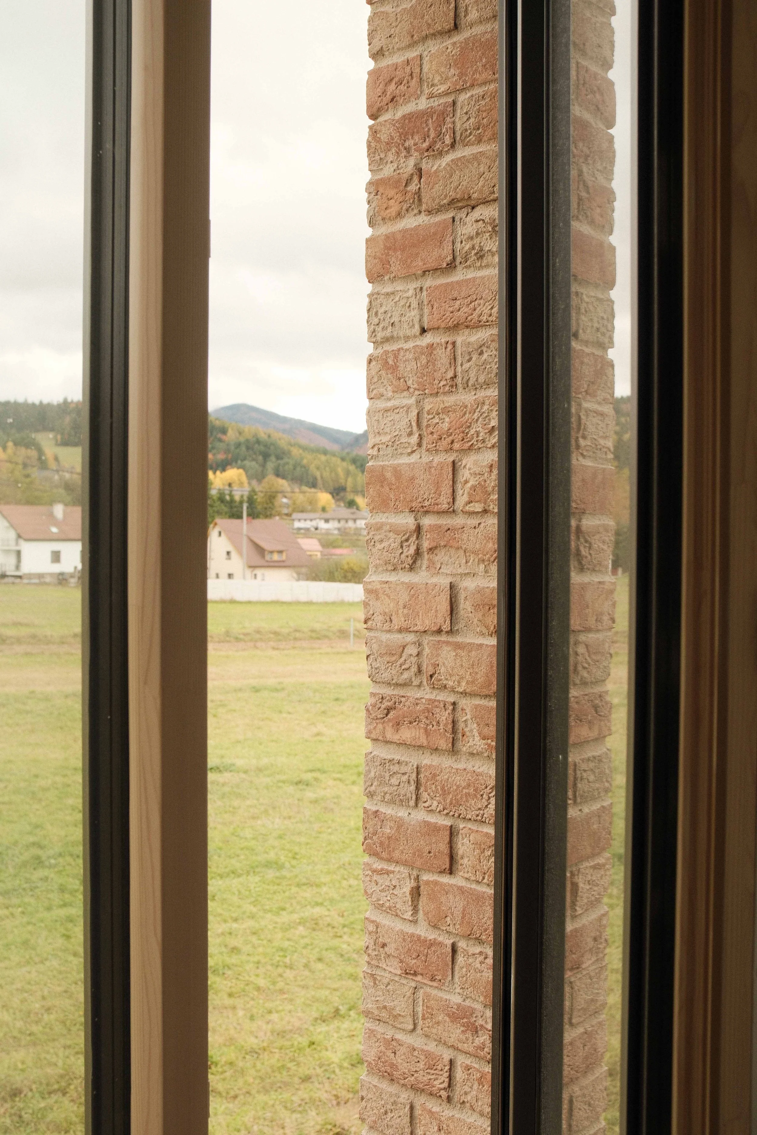 View through a window showing a rural landscape with houses, fields, trees, and a mountain in the distance.