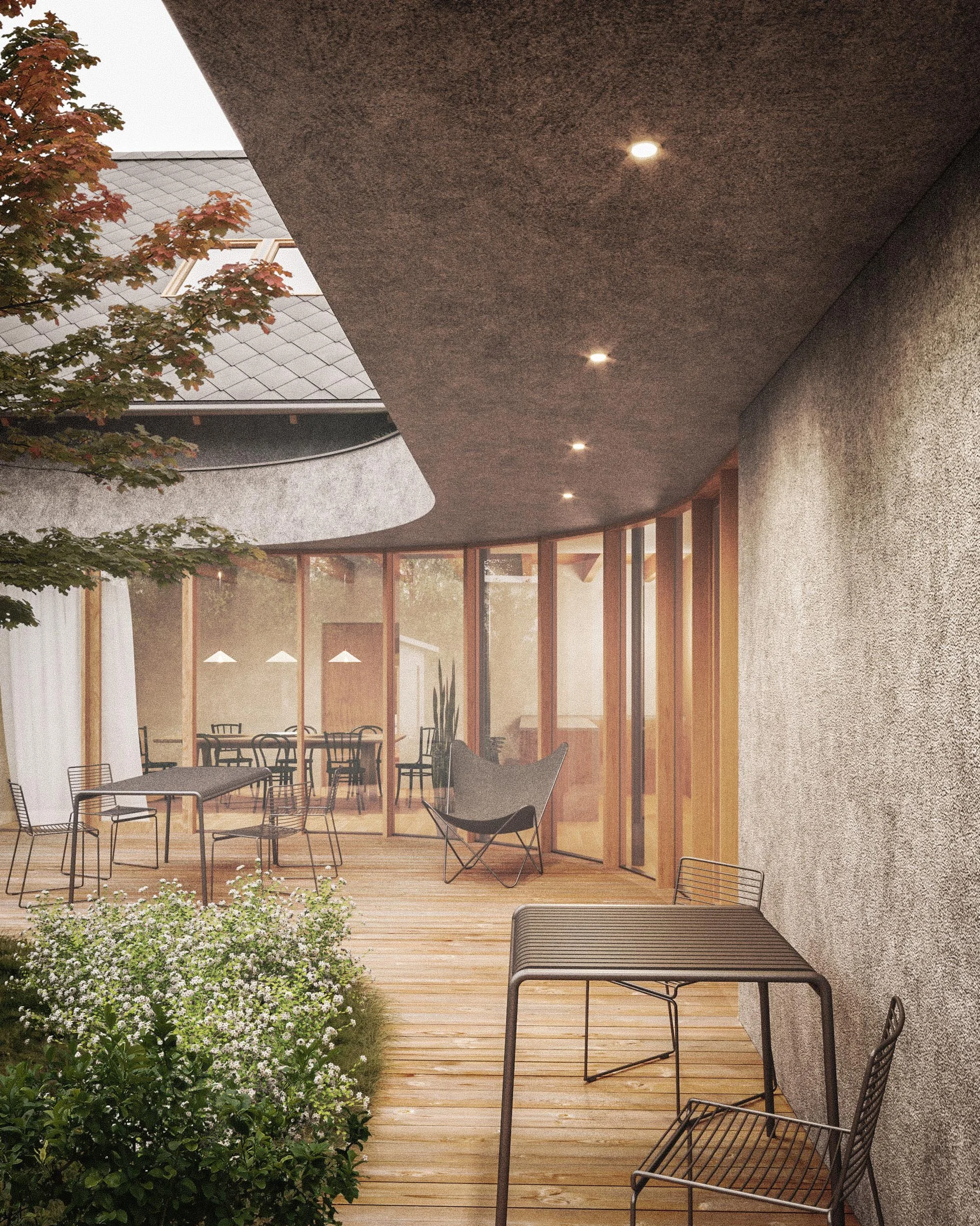 A modern outdoor patio with a wooden deck, black metal chairs, and a garden with green plants and white flowers. There is a building with a curved roof and large windows with wooden framing, and the roof has recessed lighting.