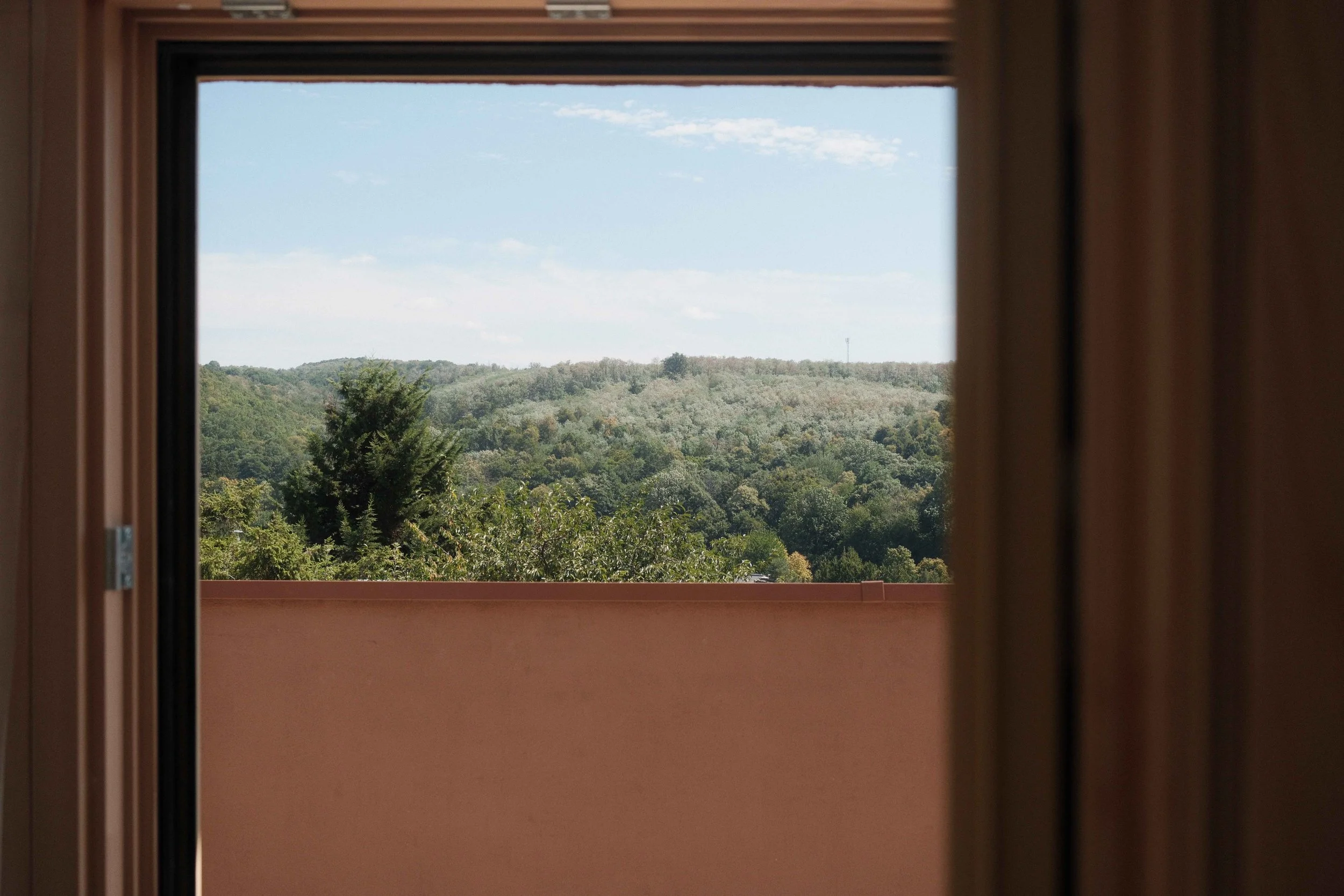 View of green wooded hills and sky seen through a window.