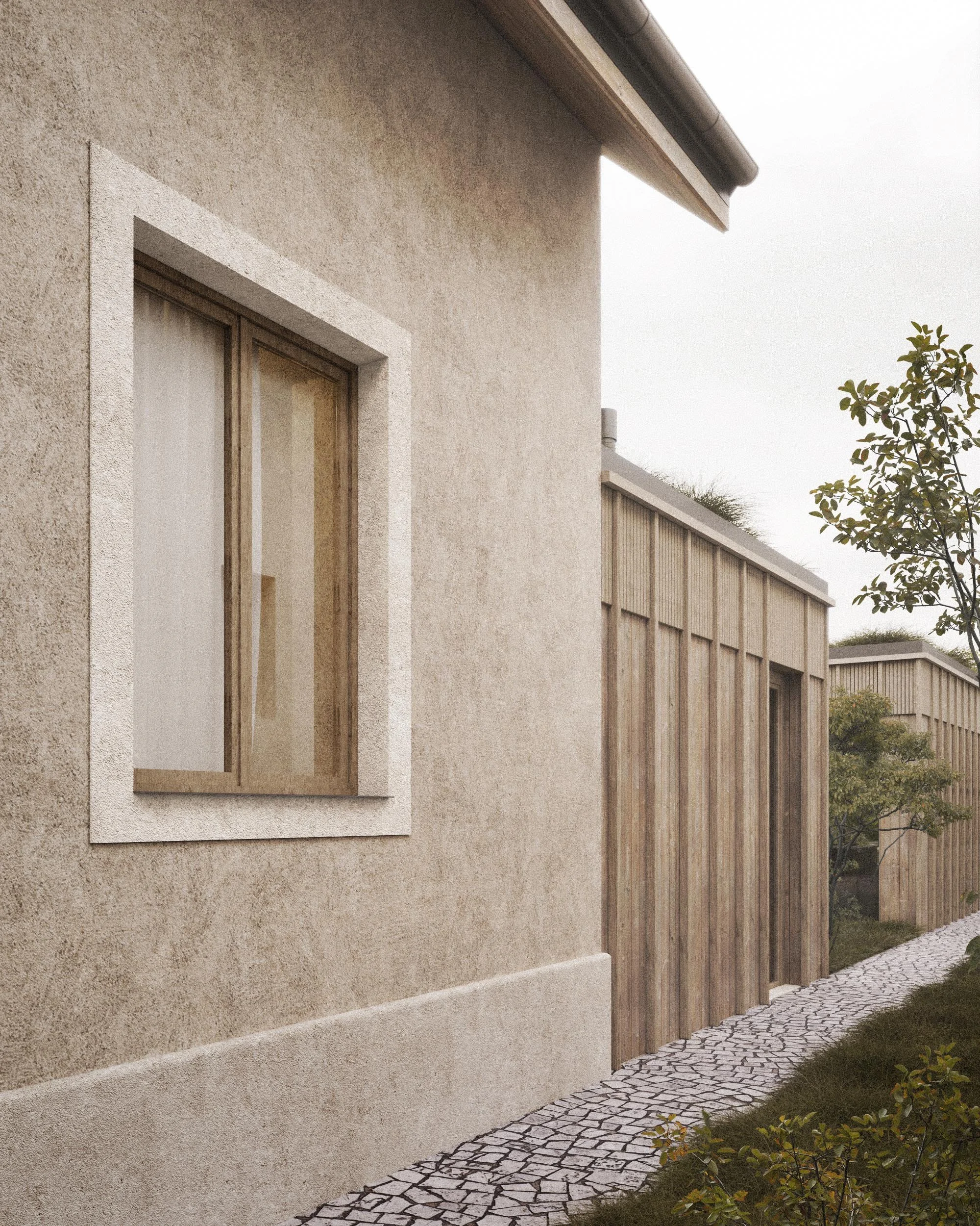 View of a modern house with beige stucco walls, a single window with a white frame, and a cobblestone pathway in the garden. The roof has a gutter and there are shrubs and trees along the side.