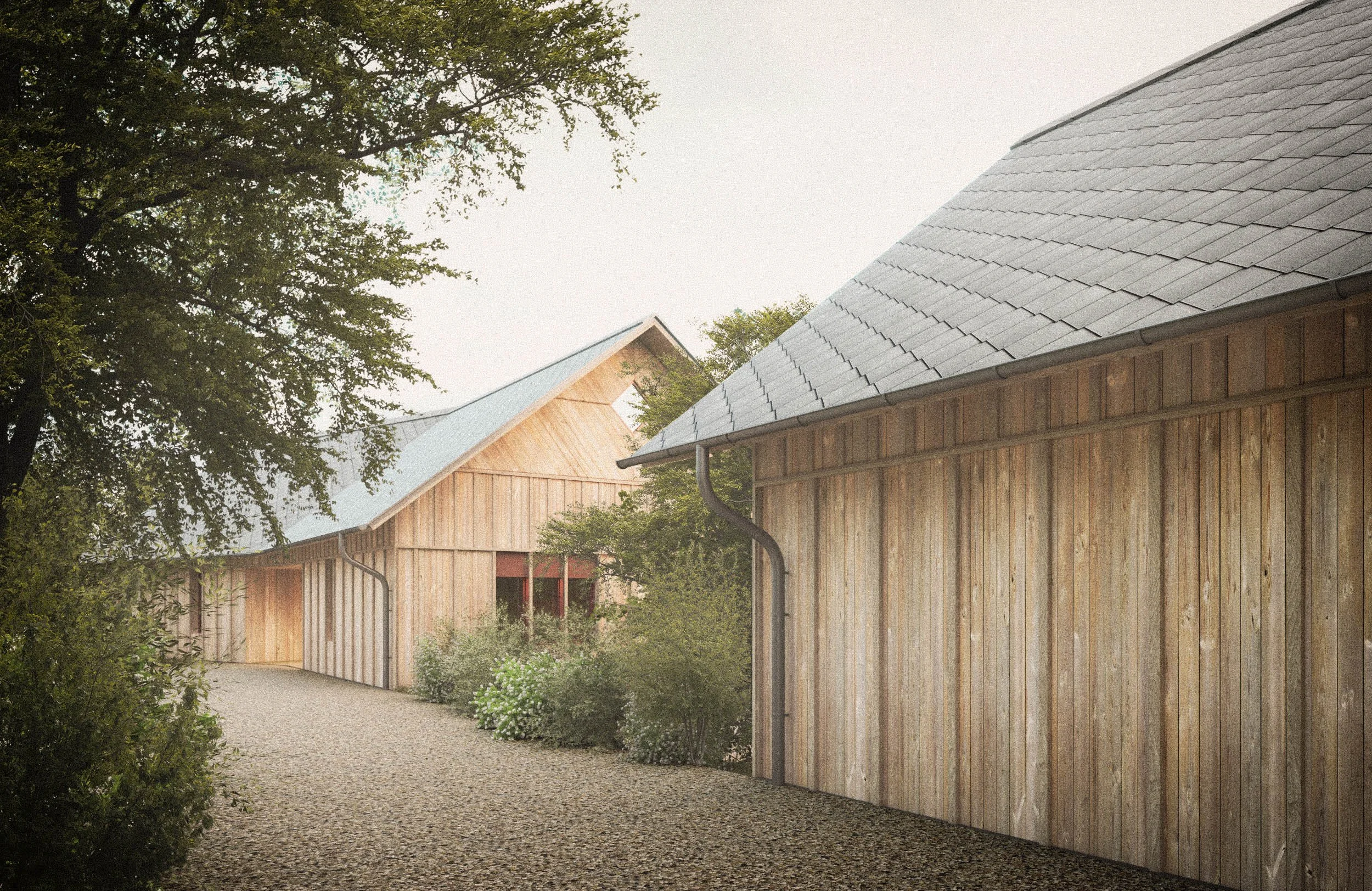 A daytime outdoor scene showing a gravel pathway beside a wooden building with a metal roof, greenery, and trees in the background.