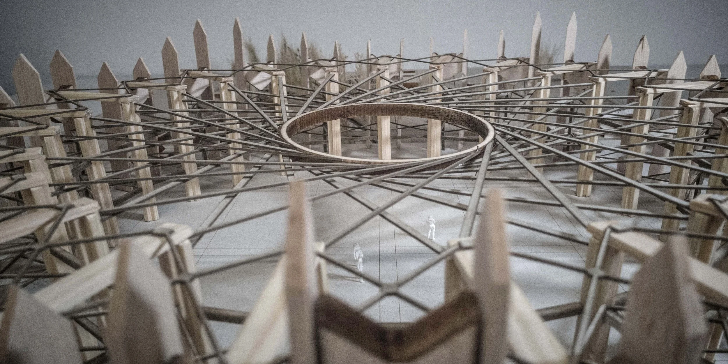 Architectural model of a circular structure with wooden and metal components and small human figures for scale.