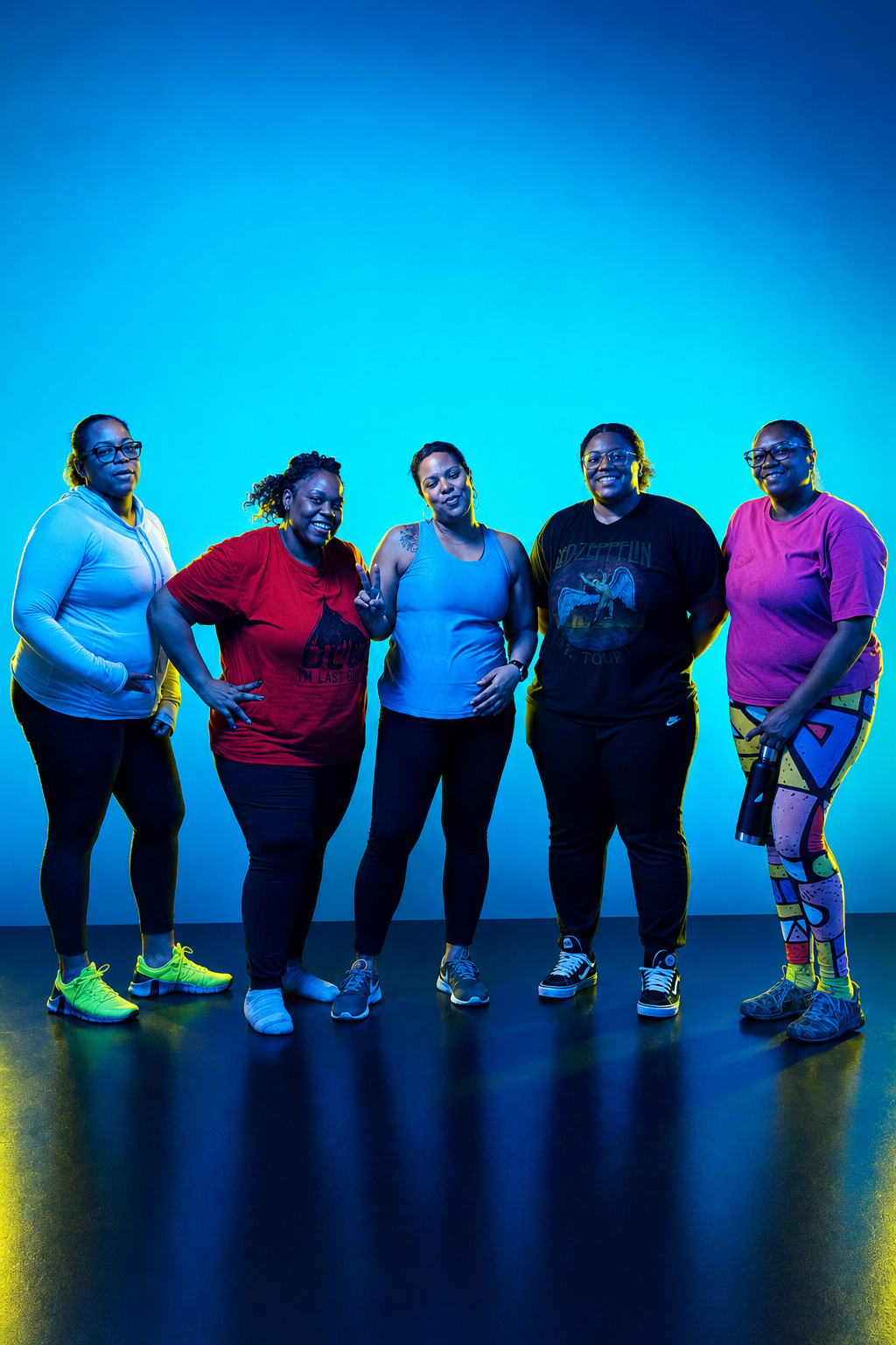 Group of five diverse women dressed in activewear, standing together in a fitness studio with blue lighting.