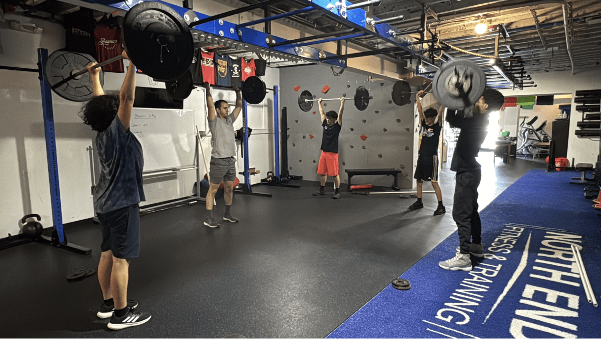 Six people exercising in a gym, lifting weights and doing weightlifting routines.