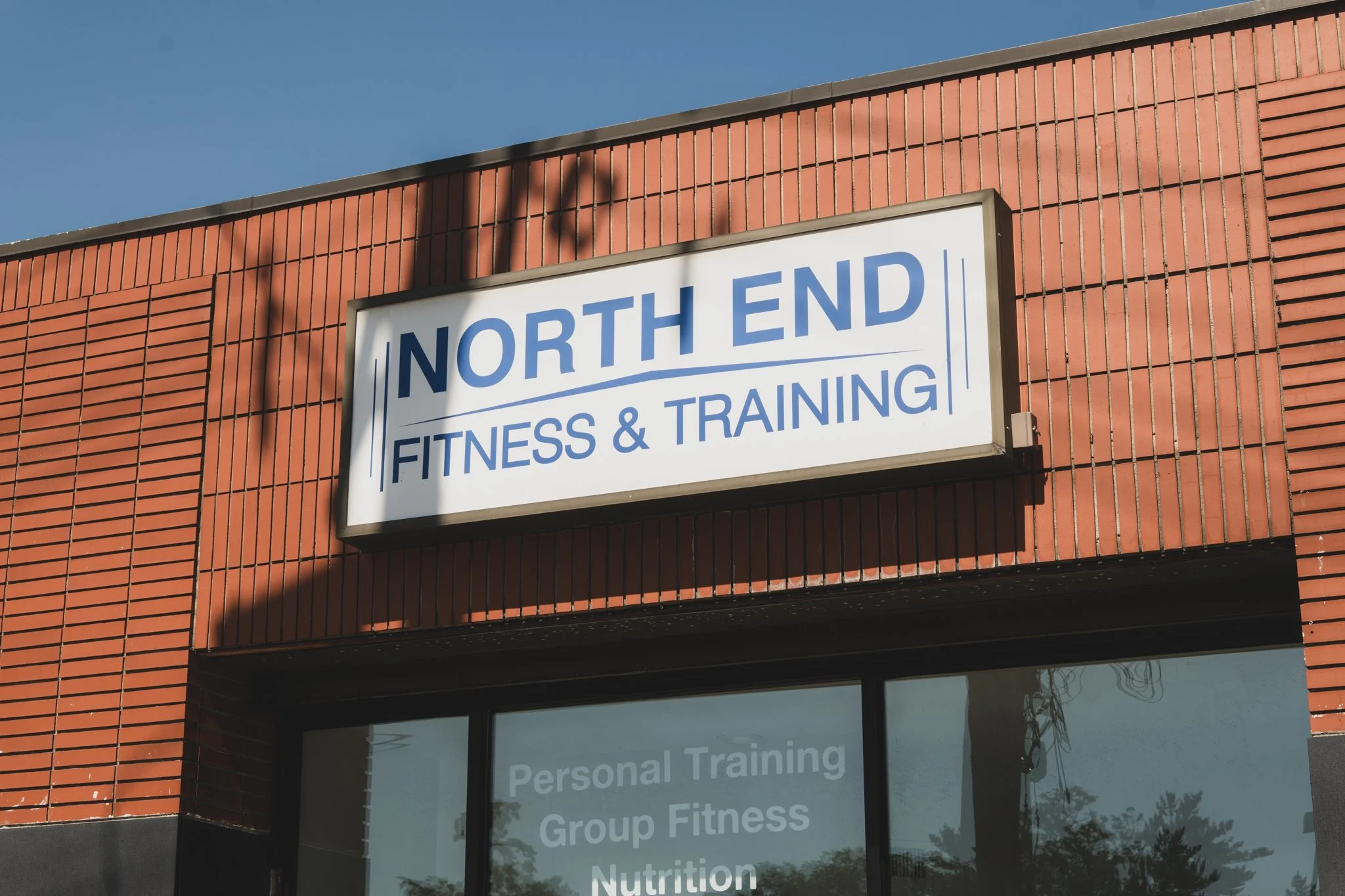 Photo of a brick building with a sign that reads 'North End Fitness & Training' and a window below with partially visible text about personal training, group fitness, and nutrition.