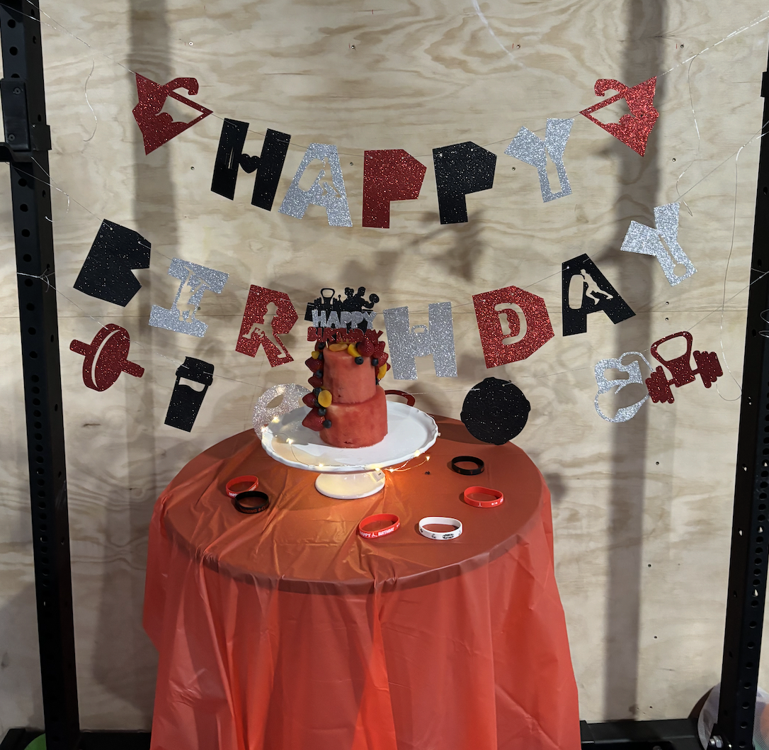A birthday party setup with a soccer-themed cake on a white cake stand, decorated with blueberries, raspberries, and candies. Behind the cake is a black top hat with