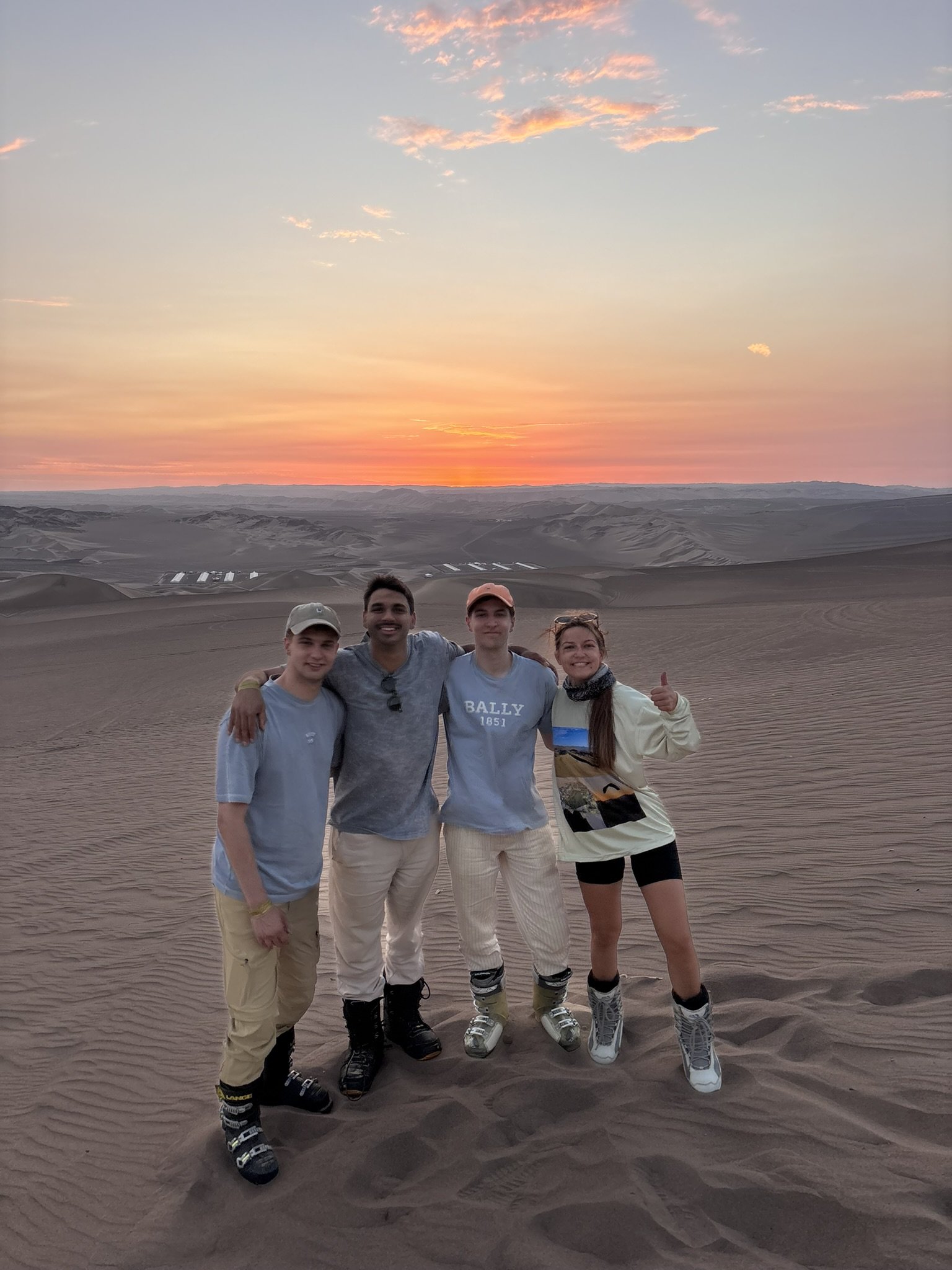 Grupo de cuatro personas en un desierto durante el atardecer, con arena y dunas en el fondo.