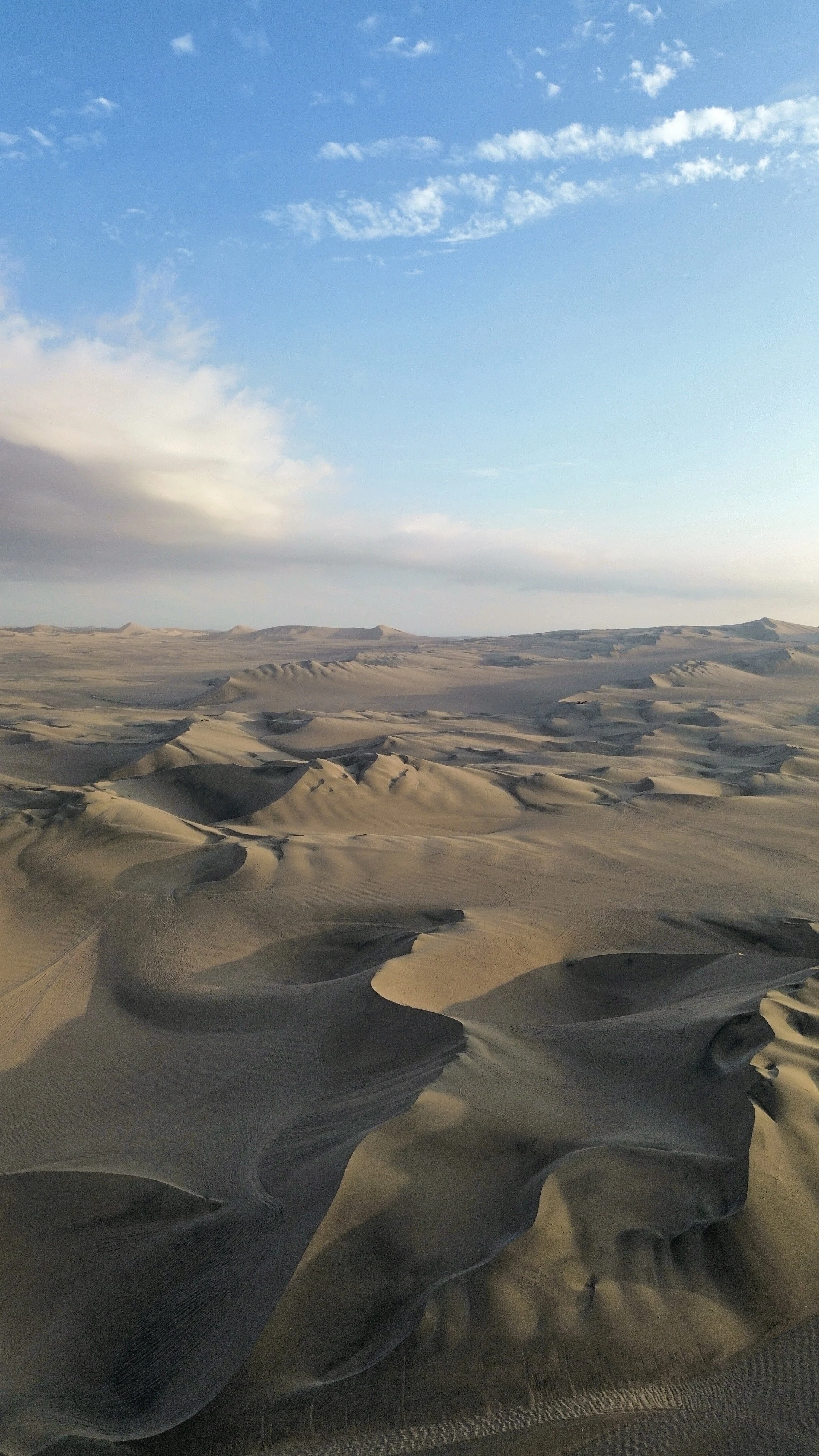 Dunas en un desierto con cielo despejado y algunas nubes.
