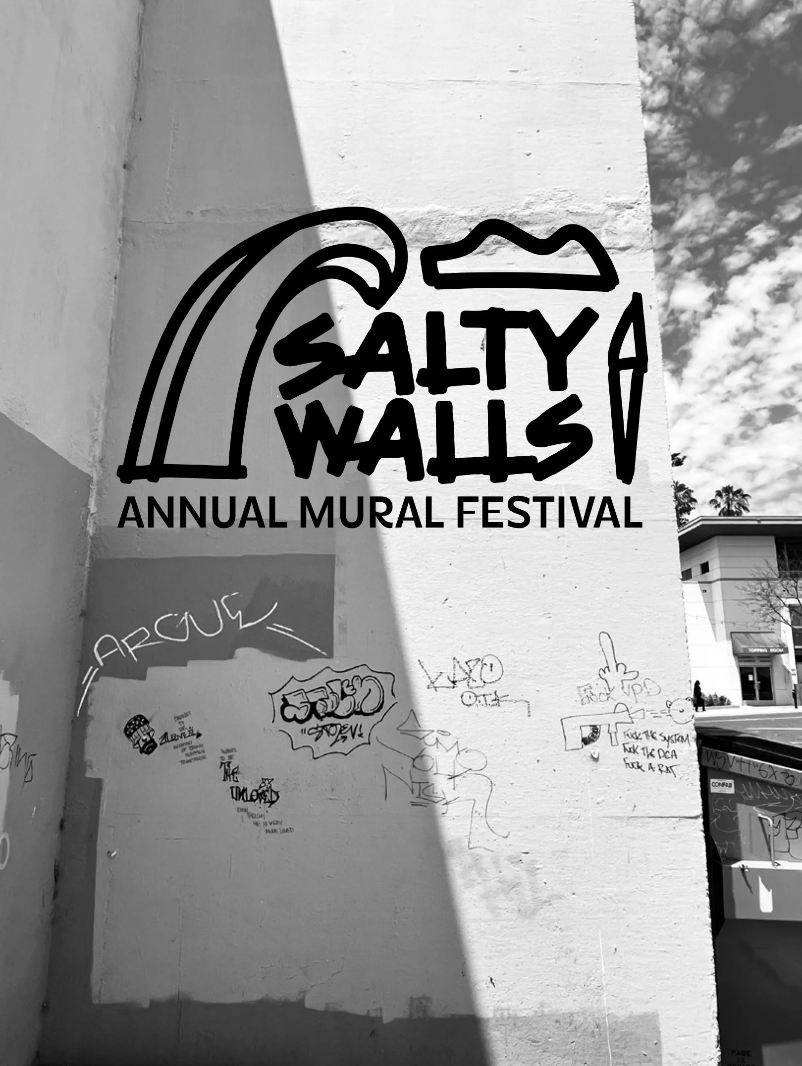 A large mural on a white wall reads "Salty Walls, Annual Mural Festival" with a cloud sky and a few trees visible in the background.