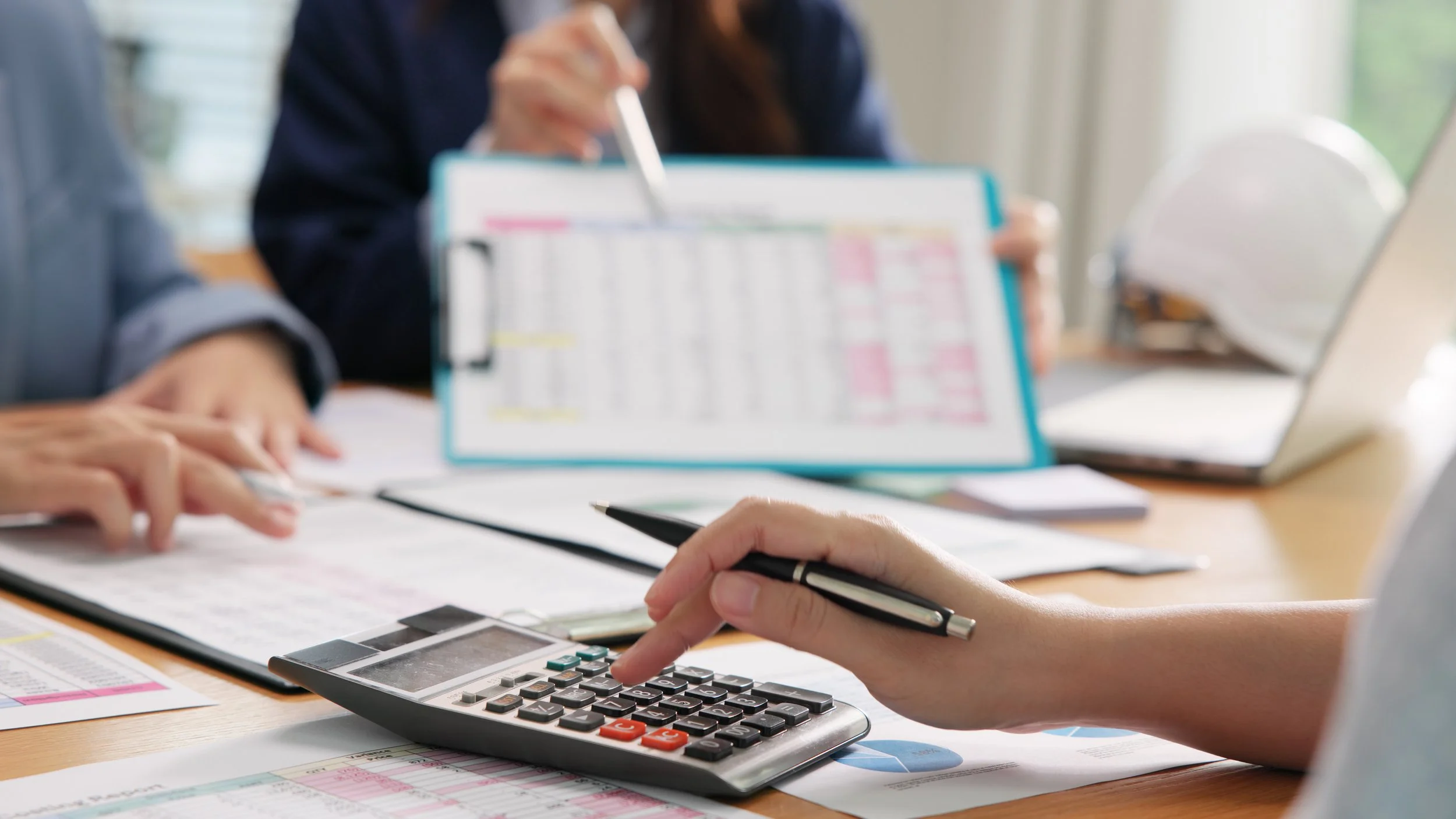 Business people at a desk with only their hands in frame. One person is pointing at a document while the other is typing on a calculator.