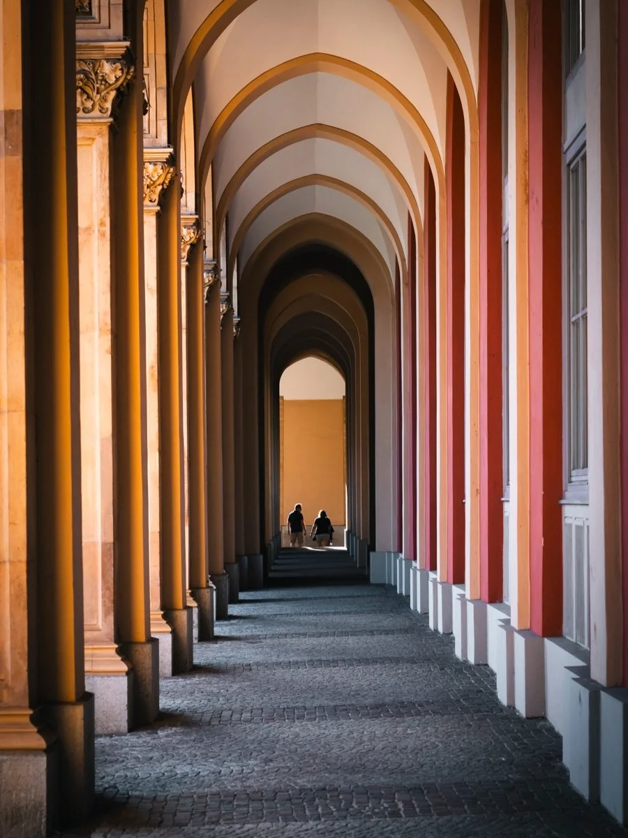 Munich builds its shade into the architecture.

Long arcades, arches folding into each other, a bit of sun getting through wherever the columns let it. Walked one afternoon looking for nothing but lines, and kept finding people small inside them.

Th