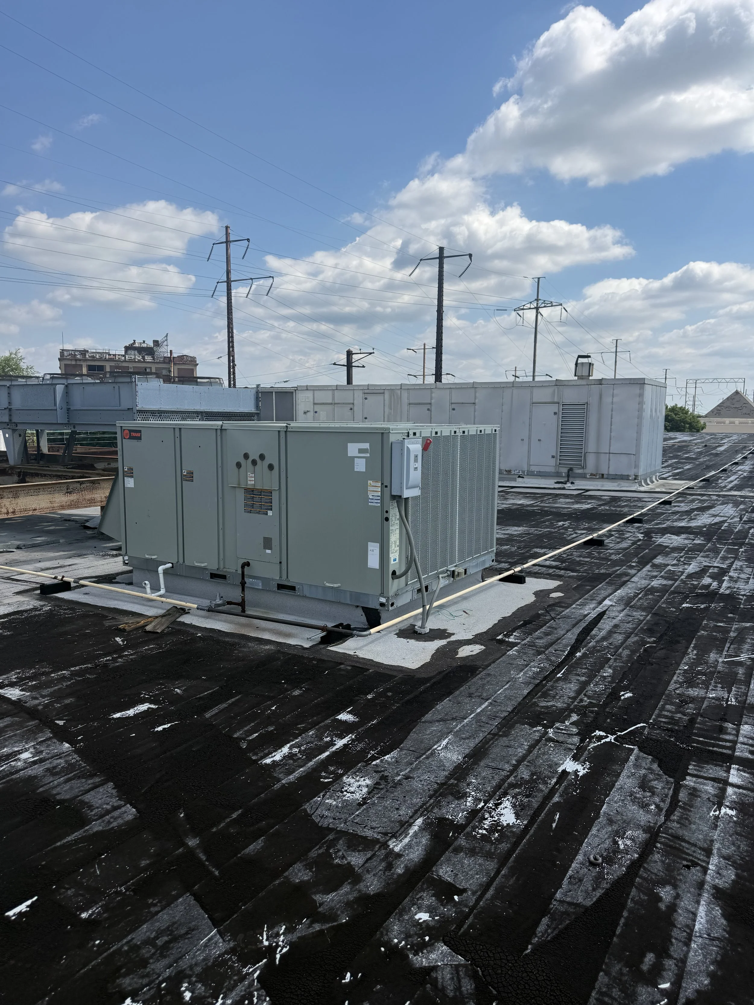 Rooftop with HVAC equipment, electrical wires, and a blue sky with scattered clouds.