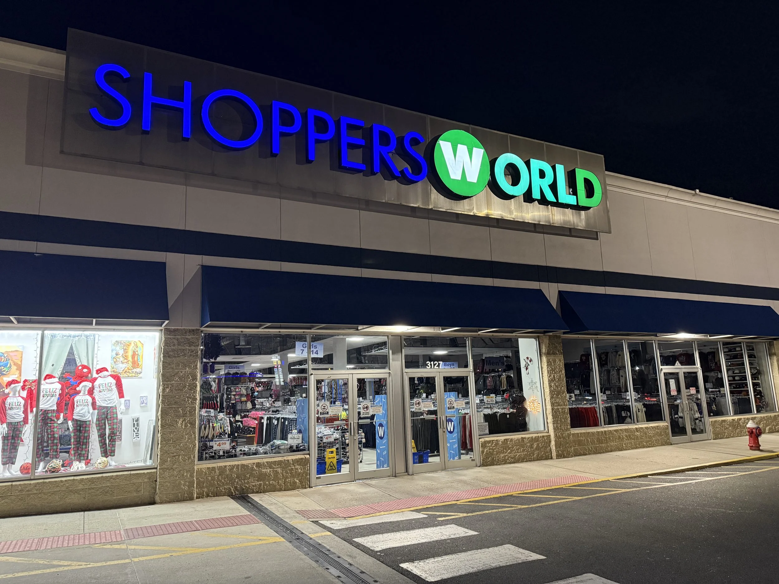 View of a Borders World store entrance at night with illuminated blue and green signage. Inside, displays of clothing and holiday decorations are visible through large glass windows.