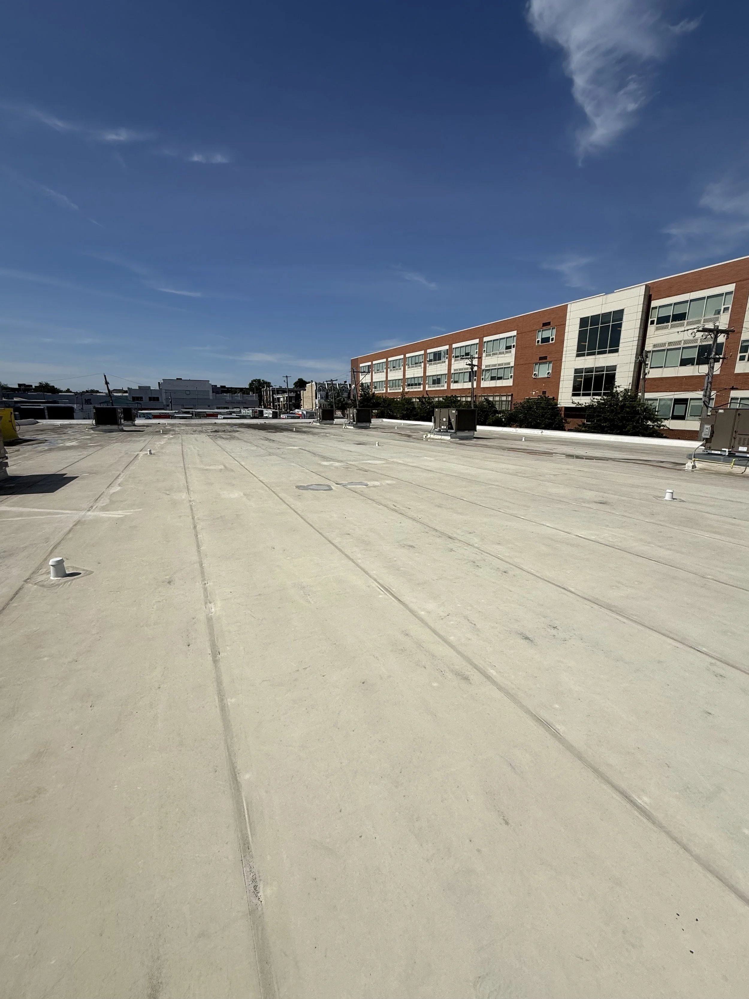 Flat rooftop with HVAC units, surrounded by buildings and power lines, under a clear blue sky with some clouds.