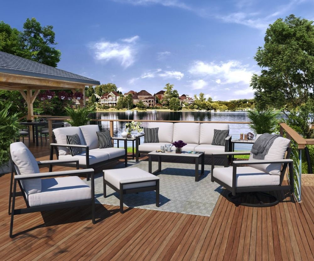 Outdoor patio with white cushioned furniture, a coffee table, and a view of a lake, trees, and houses in the background.