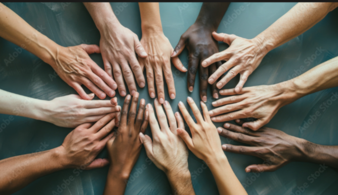 Multiple hands of different skin tones placed together in the center of a table.