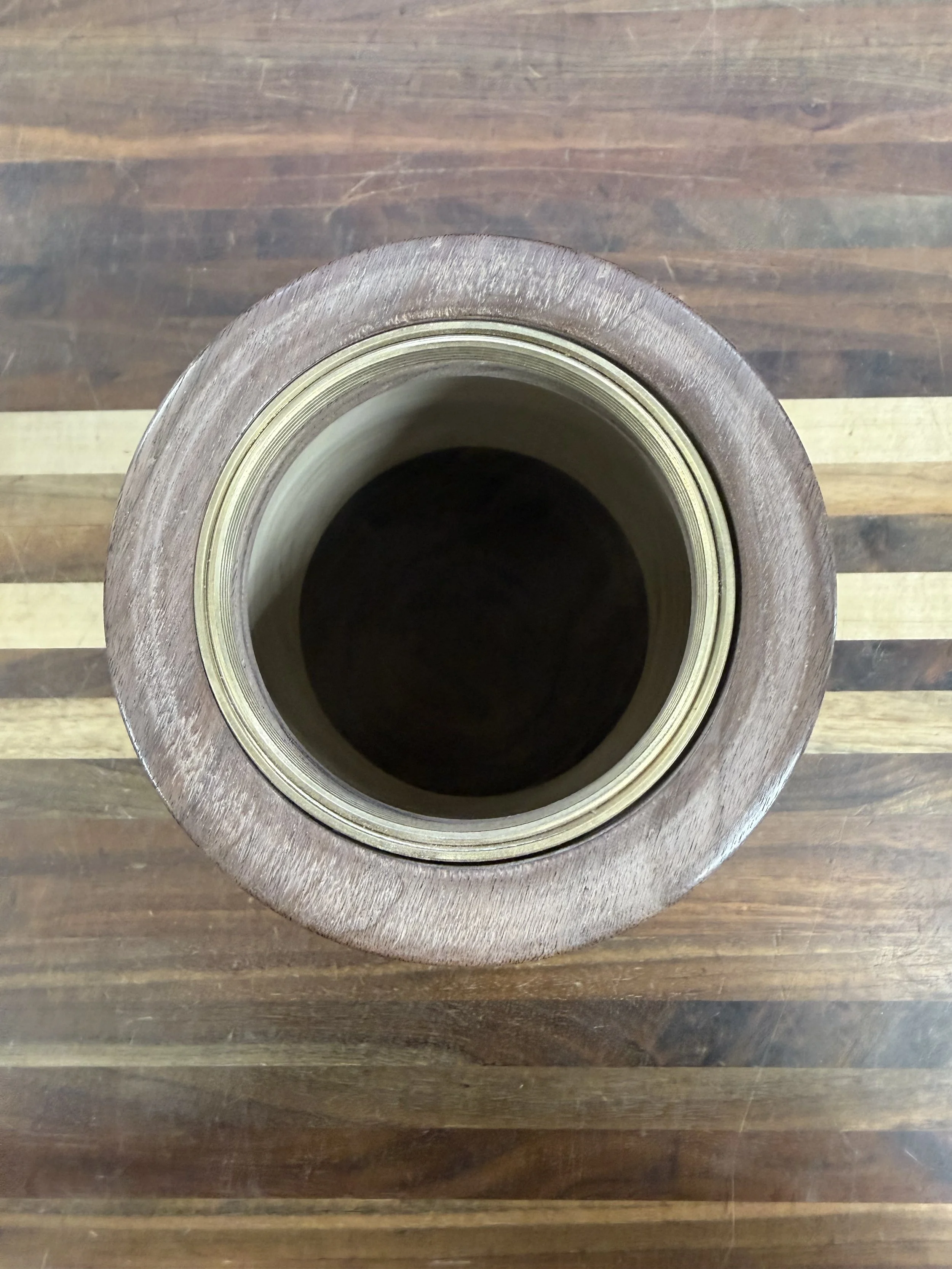 A roll of brown packing tape with a clear center, placed on a wooden surface with dark and light wood stripes.