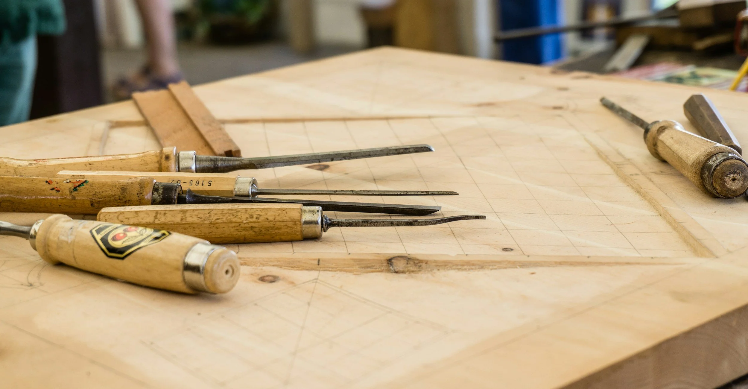 A woodworking workbench with various chisels and carving tools laid out on it in a woodworking shop.