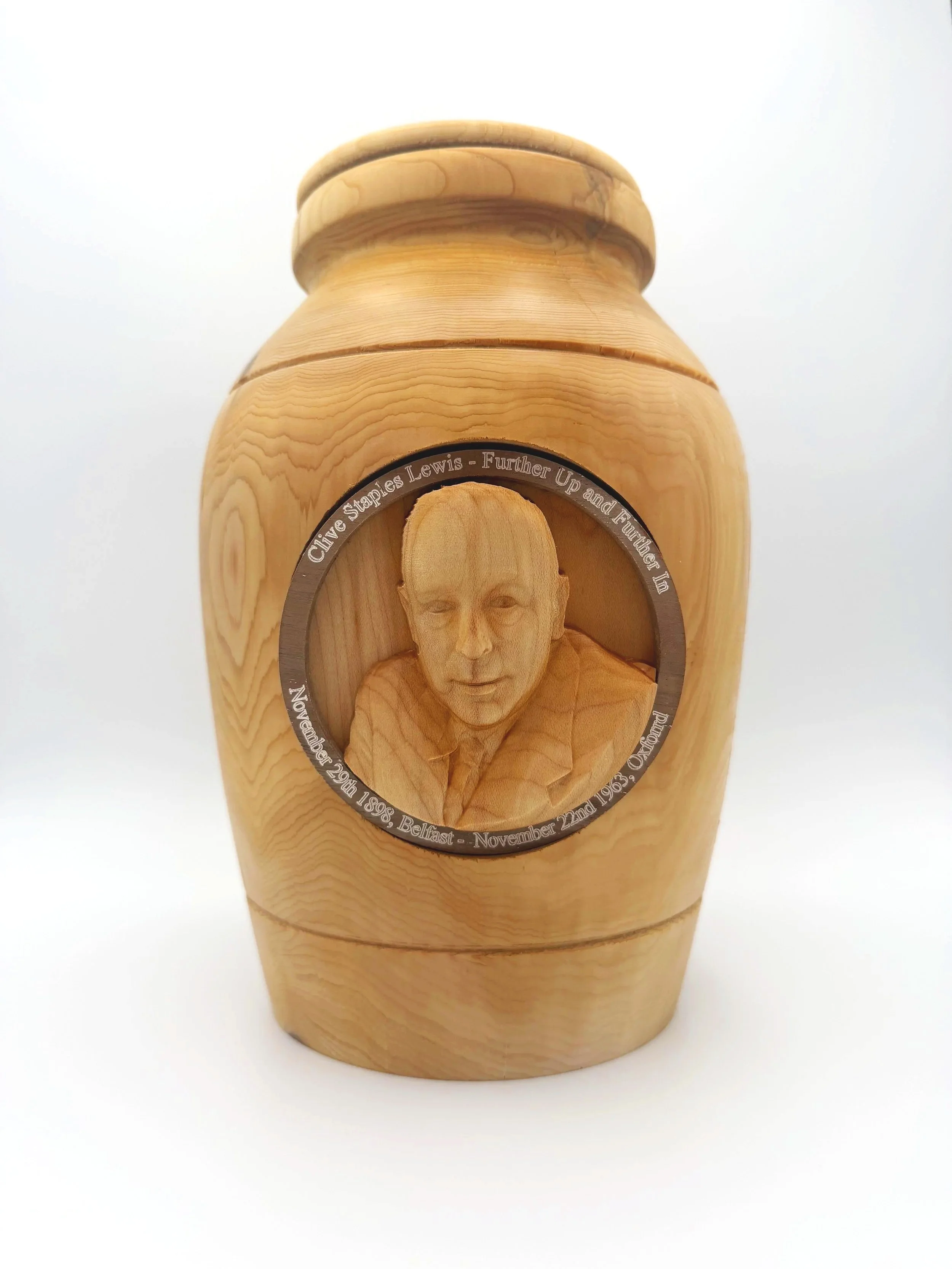 Wooden urn with a carved portrait of a person's face and a metal ring with engraved text.