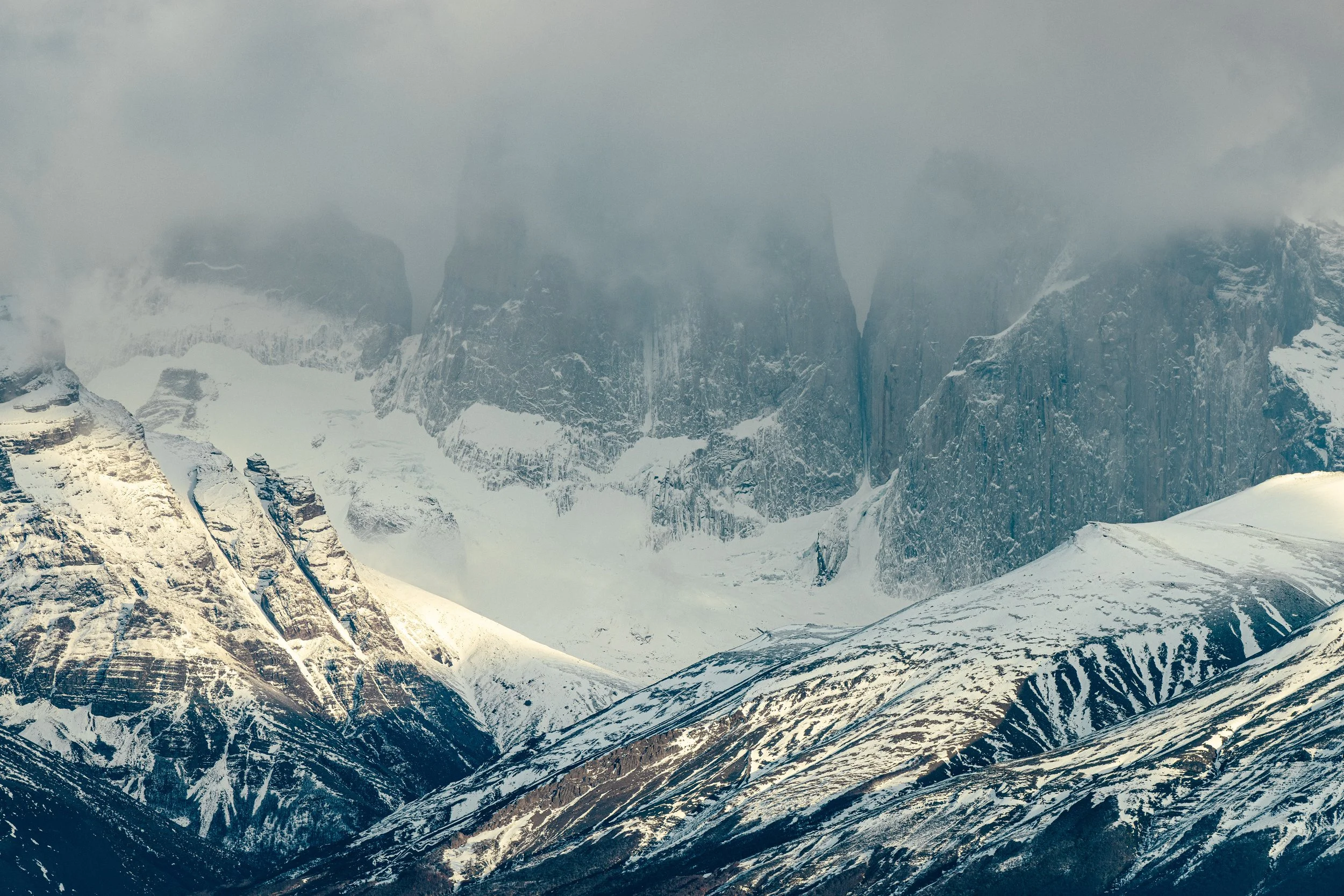 Snow-covered mountain peaks and rugged slopes shrouded in mist and clouds.
