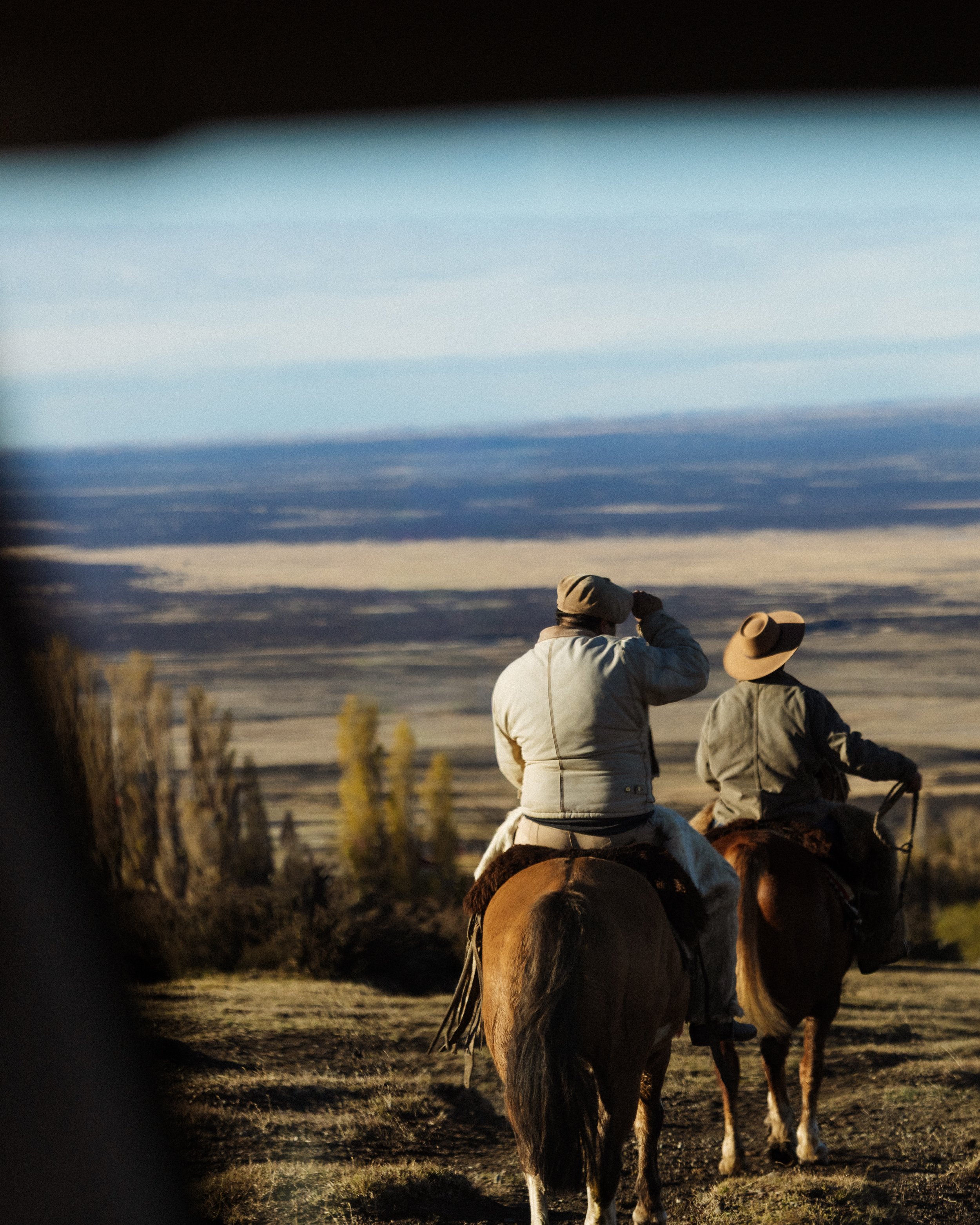 Two people riding horses through a landscape at dusk or dawn, with expansive sky and distant horizon.