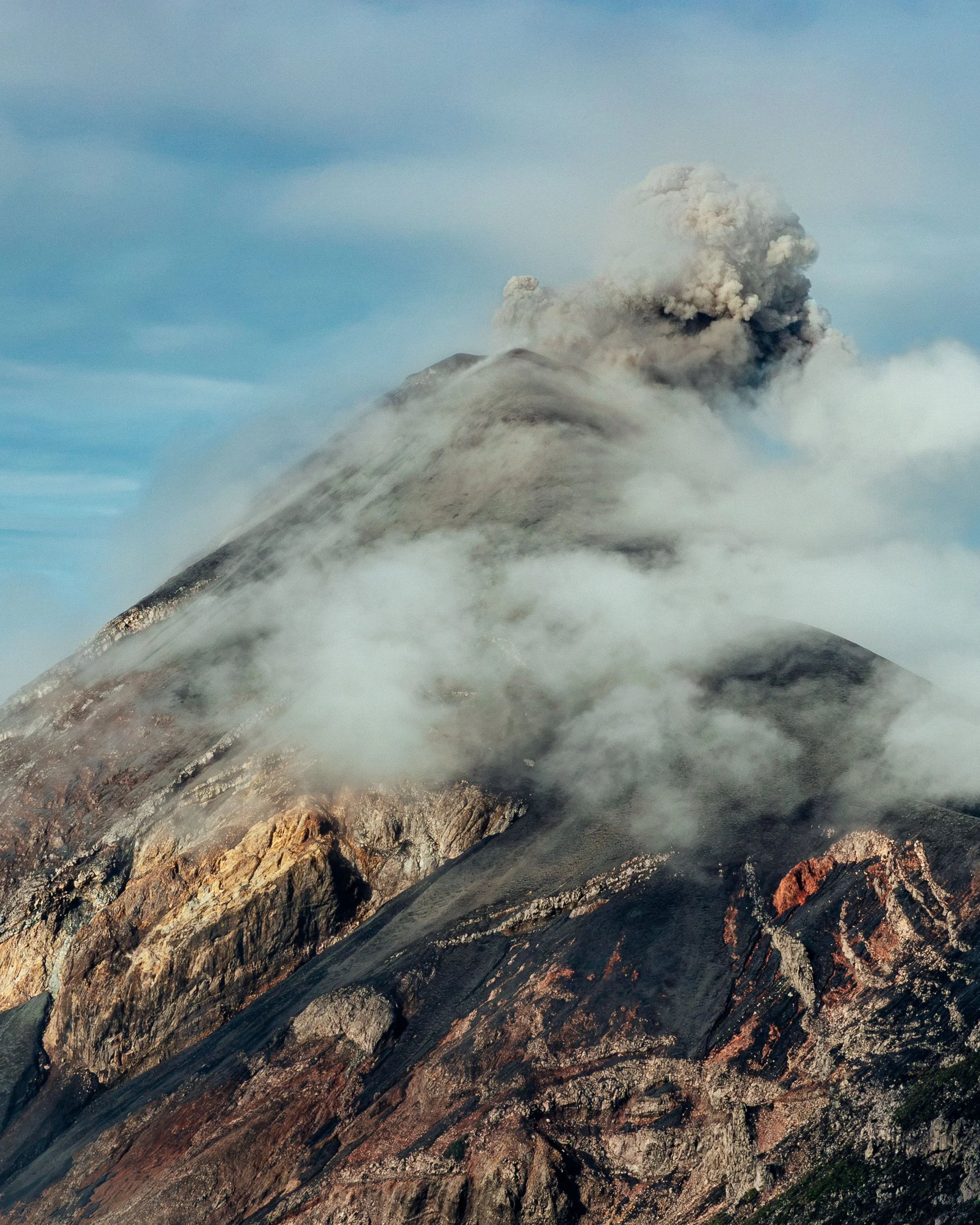 A volcano erupting with ash and smoke billowing into the sky, surrounded by rocky terrain.