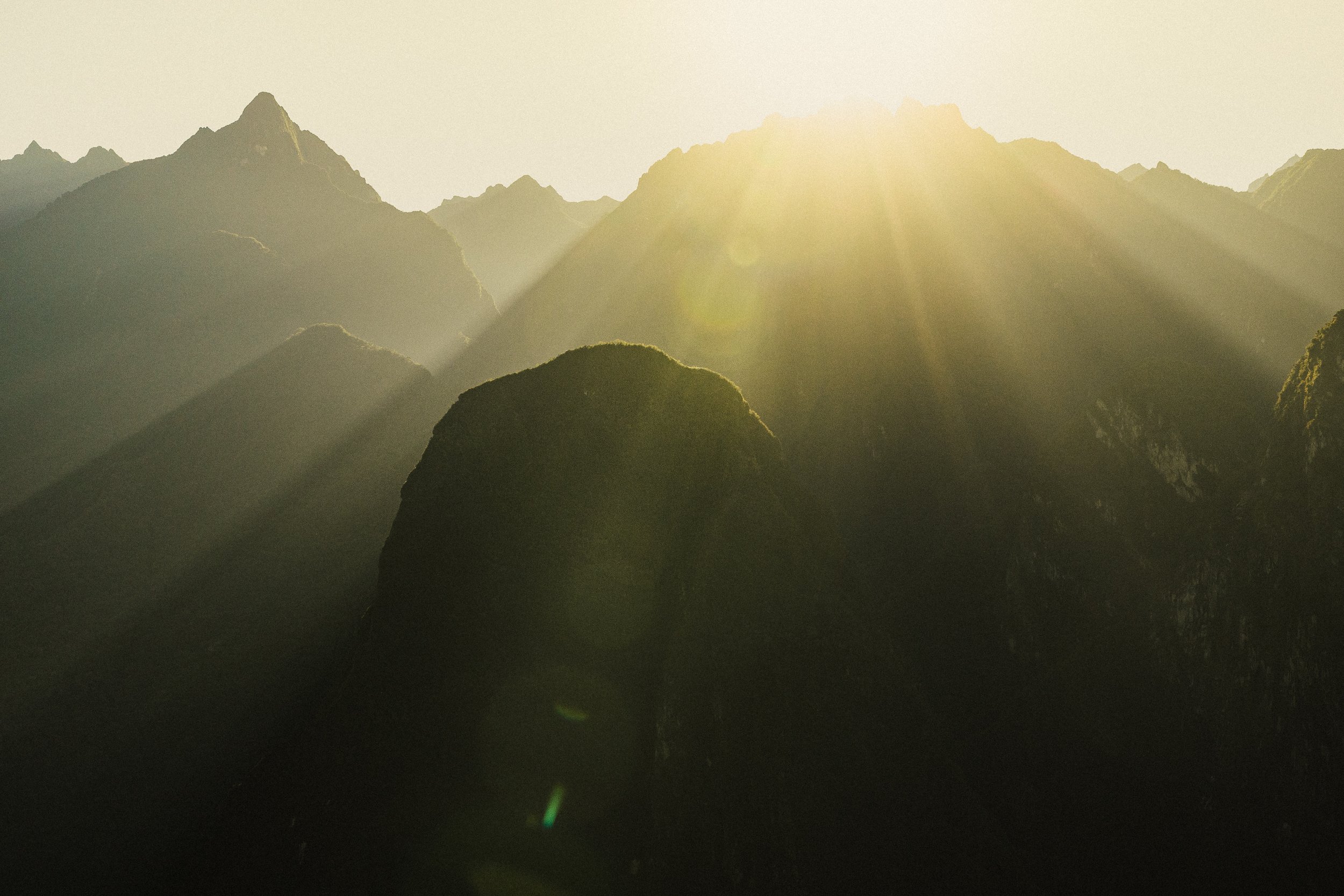 Sunrise over a mountain range with rays of sunlight shining through the peaks.
