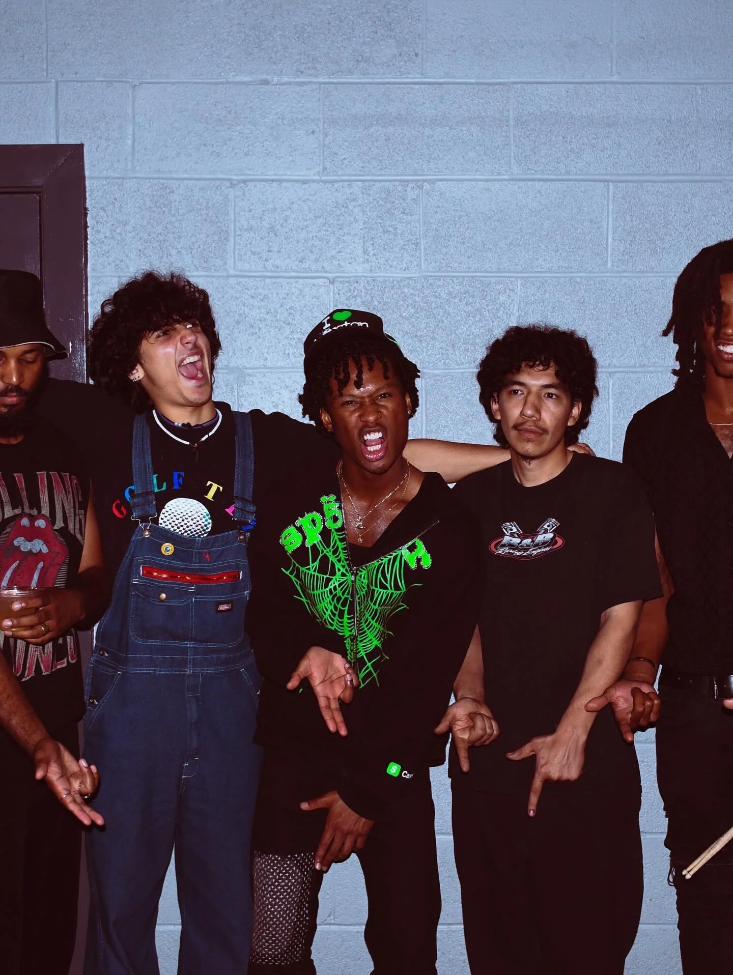 Group of five diverse people standing together against a gray brick wall, making various hand gestures and smiling.