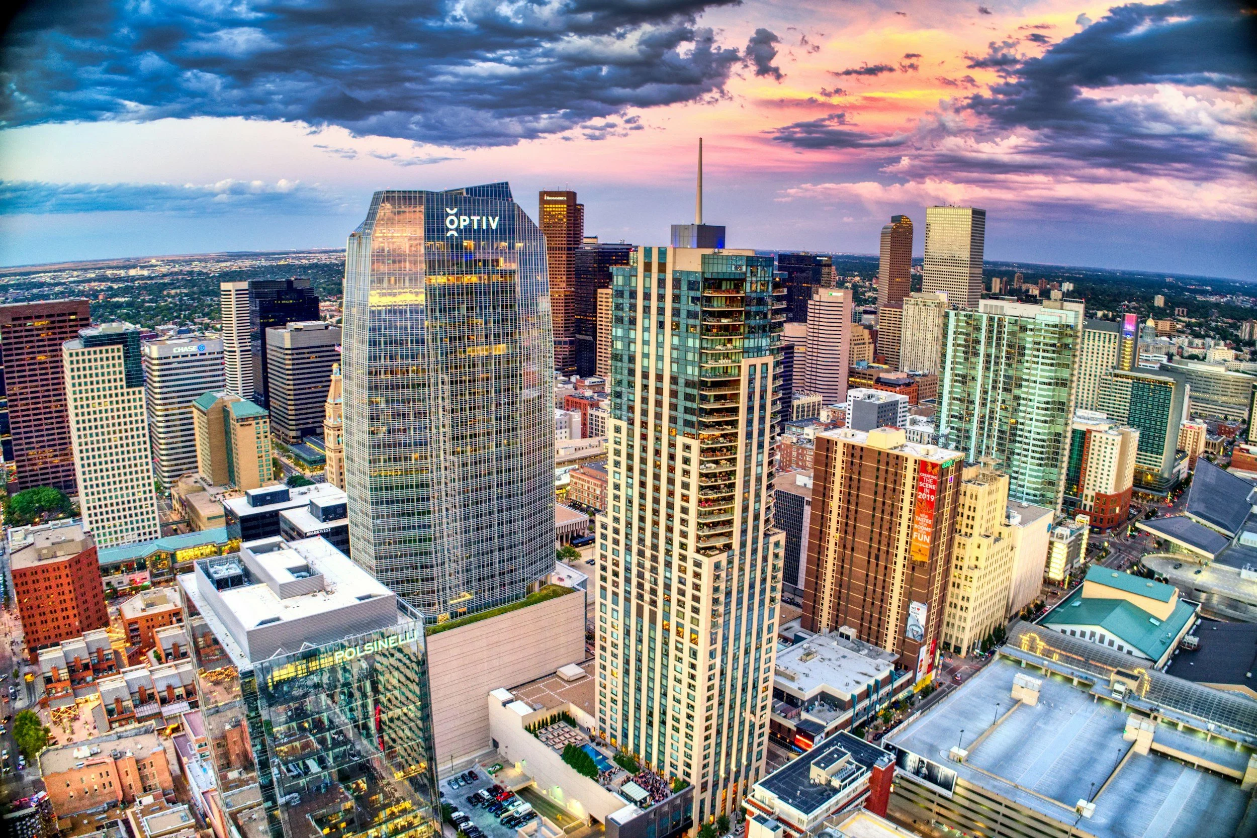 A high-rise cityscape at sunset with tall modern buildings, including the OPTIV and Polsinelli offices, under a colorful sky with scattered clouds.