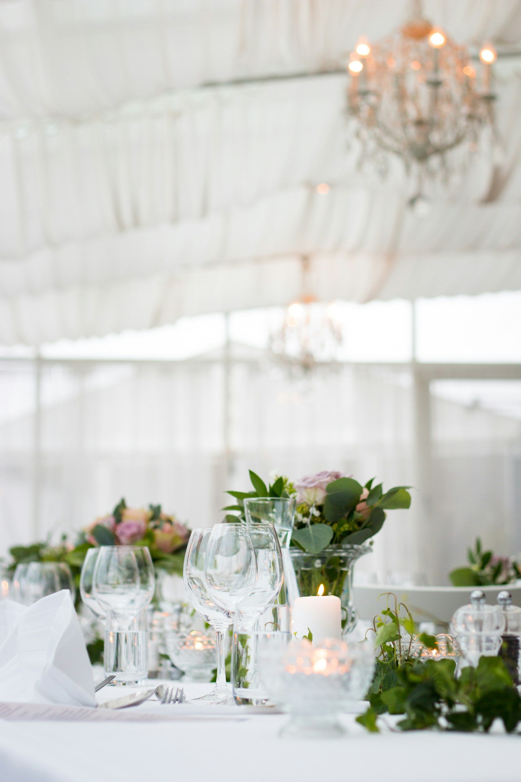 Elegant table setting with wine glasses, floral arrangements, candles, and white tablecloth at a formal event under a chandelier.