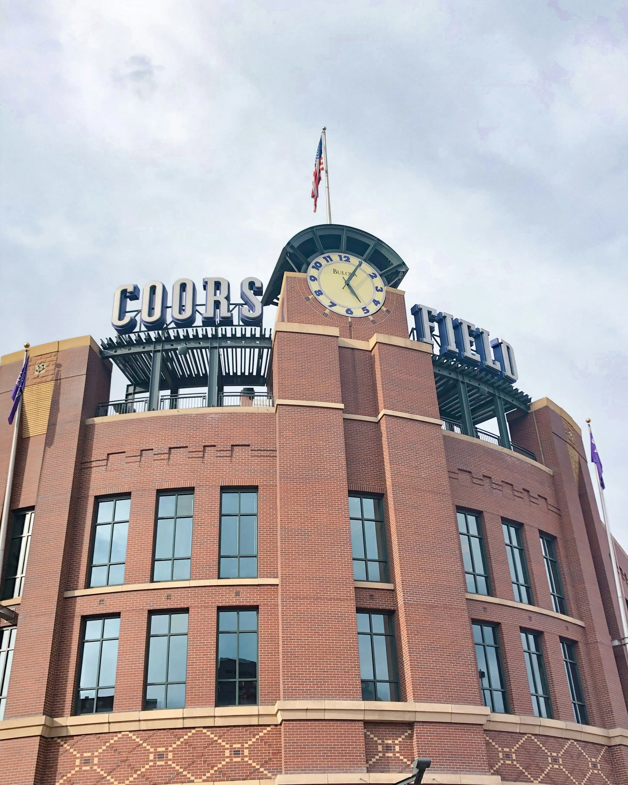 A tall brick building with large windows and a clock with the time showing 2:04. An American flag is flying on top of the building.