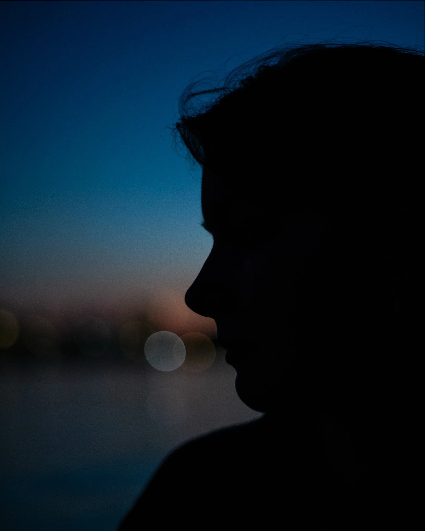 Silhouette of a person's profile against a twilight sky, with blurred city lights in the background.
