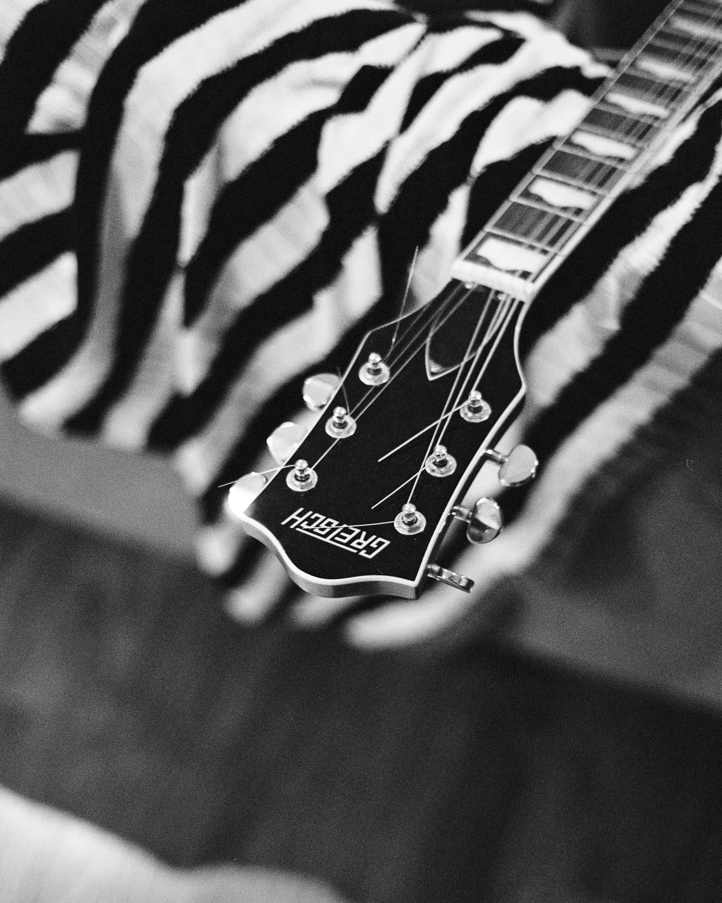 Close-up of a guitar headstock with tuning pegs and strings, partially obscured by zebra-patterned fabric or clothing.