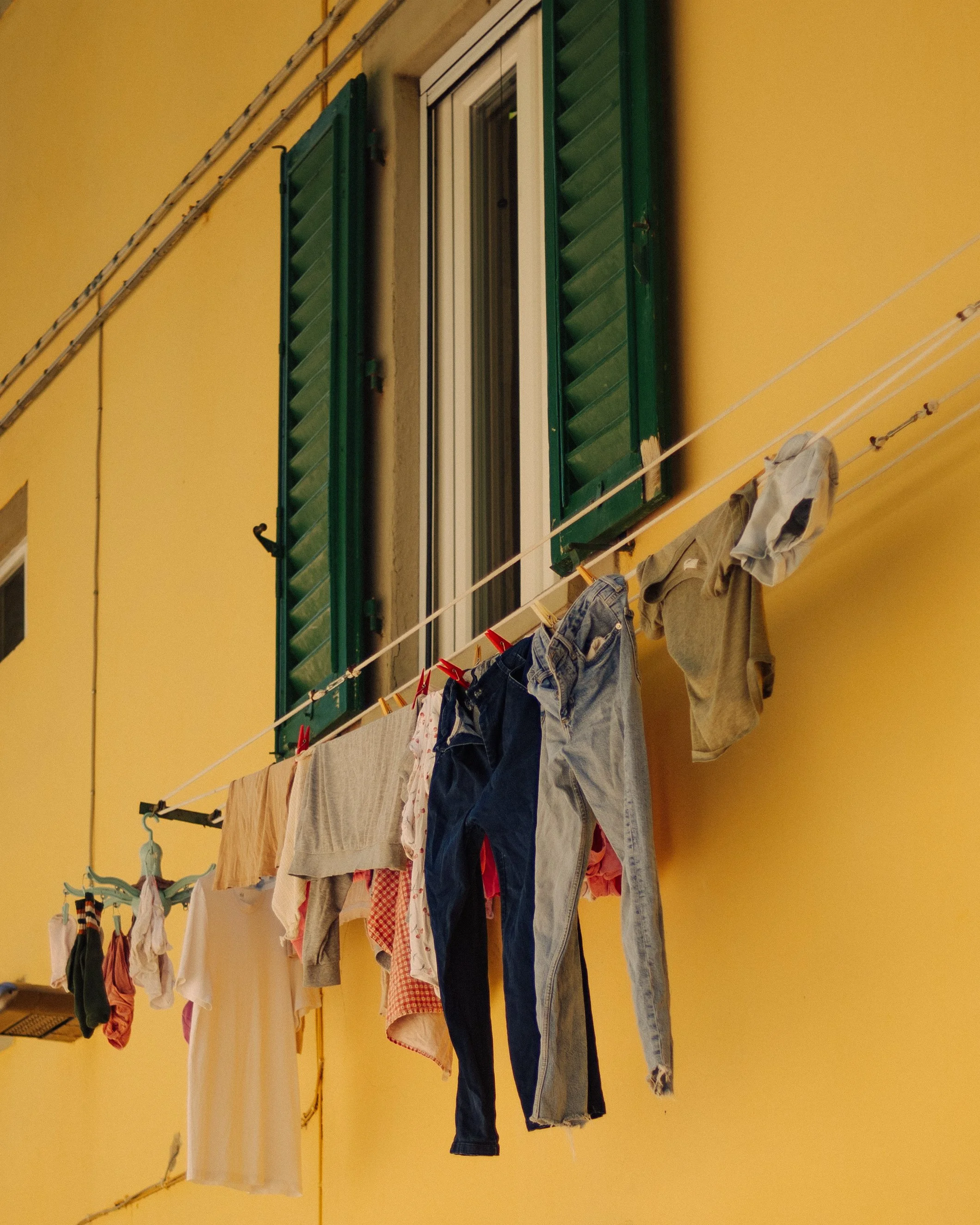 Clothes hanging on a clothesline outside a yellow building with green window shutters.