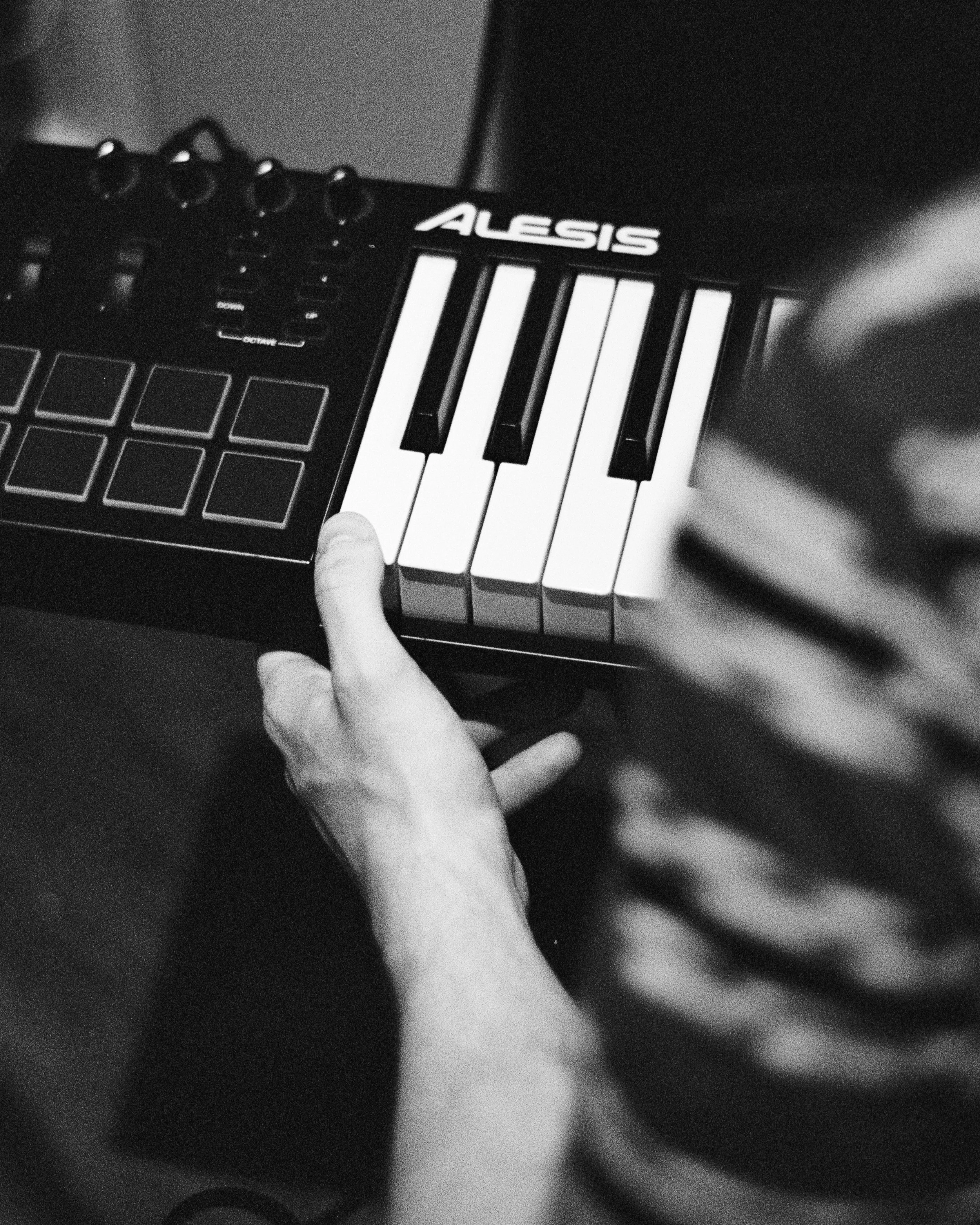 A person holding a small electronic keyboard with the brand name 'ALESIS' visible.