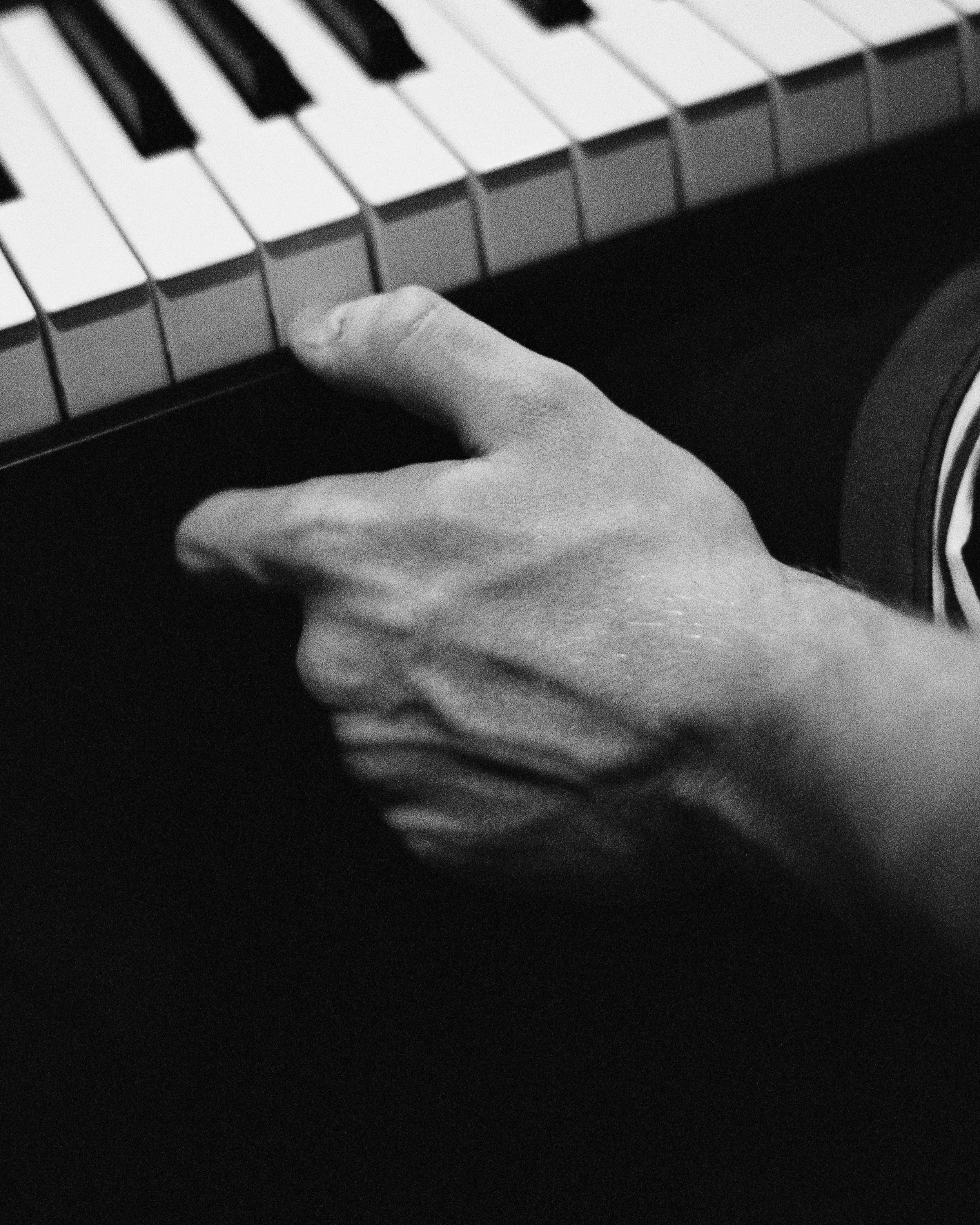 A hand playing a keyboard, with the hand covering some keys, in black and white.