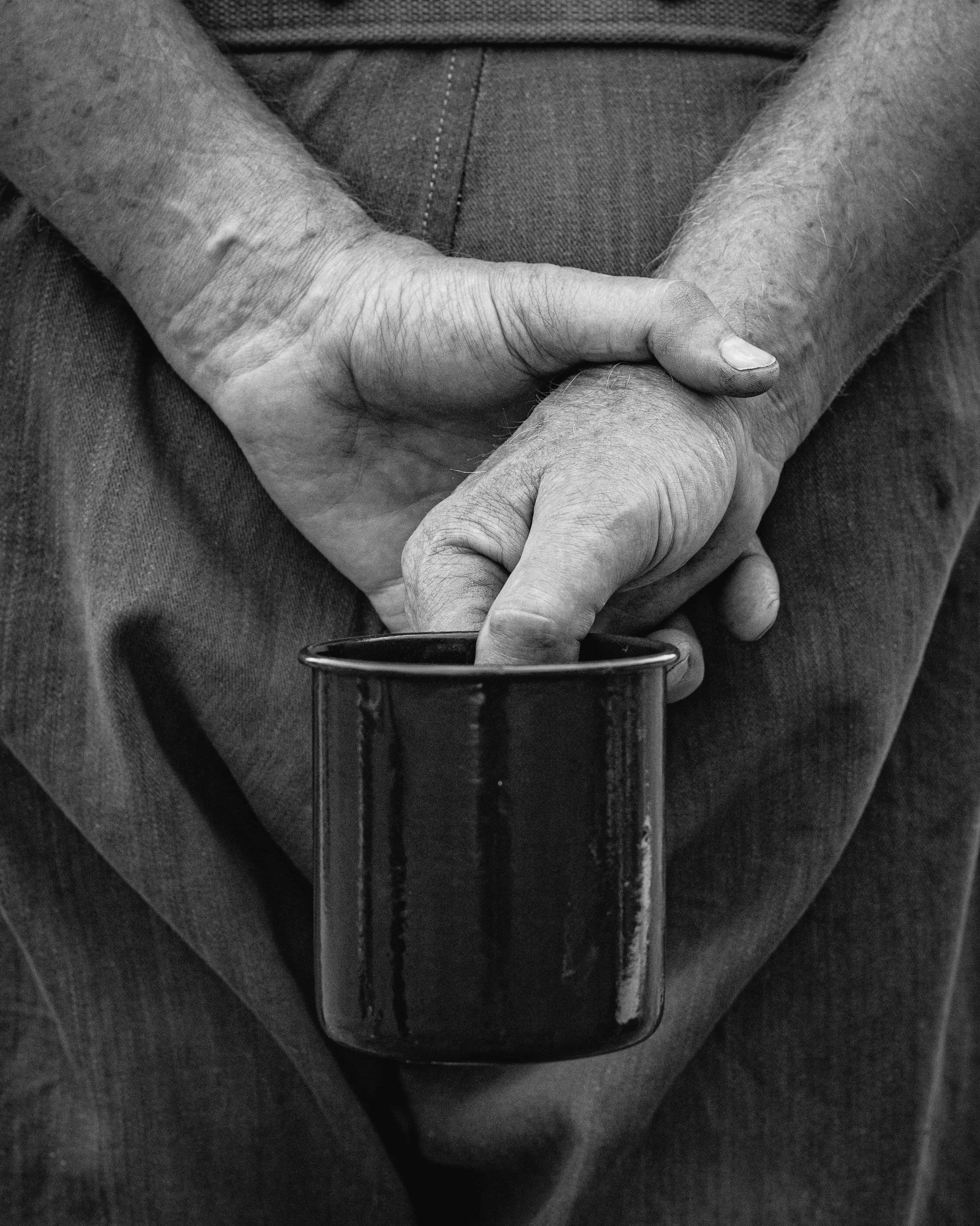 Close-up of a person holding a cup. The person is wearing a short sleeve shirt, and the image is in black and white.
