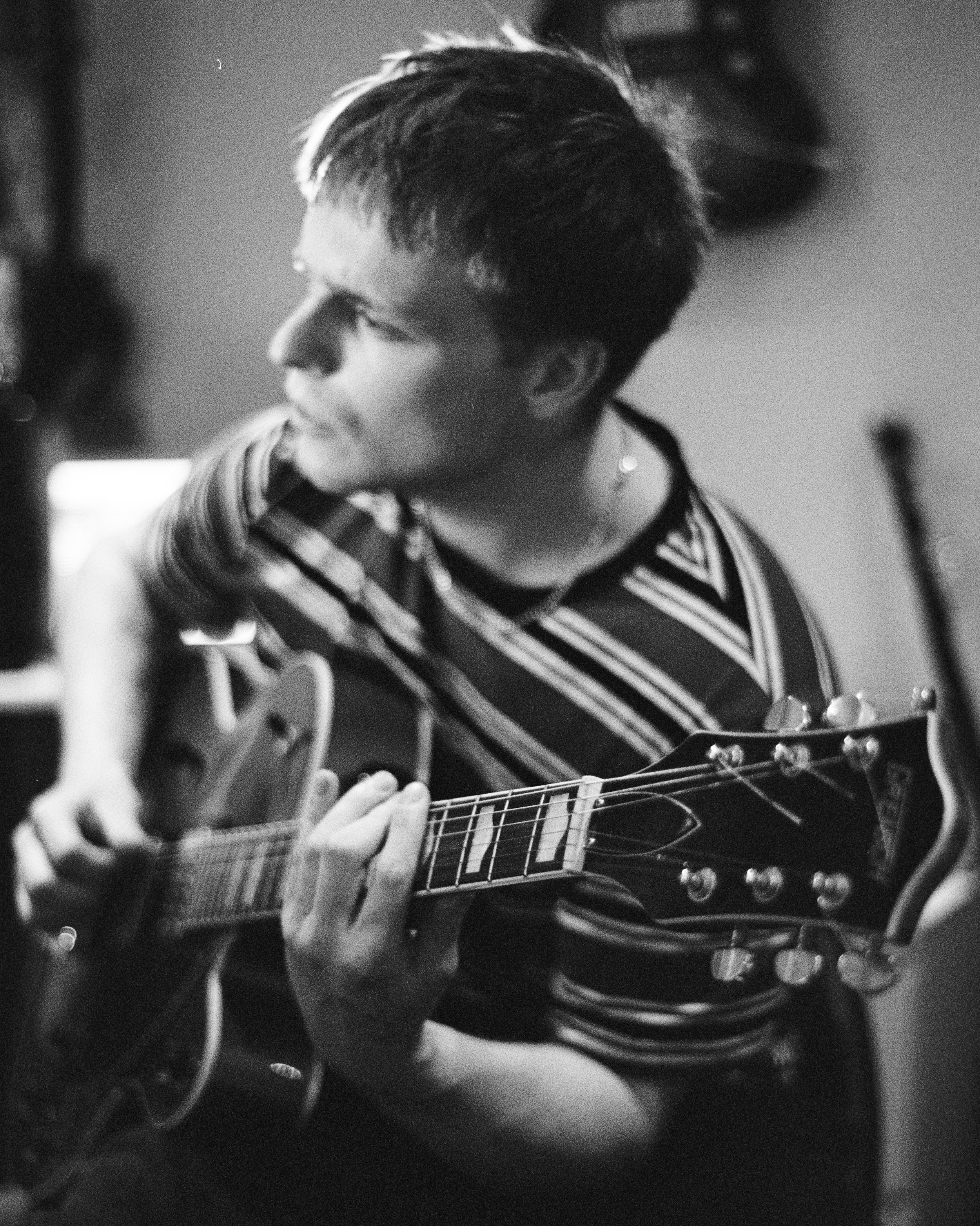 A person with short hair, wearing a striped shirt, playing an acoustic guitar.