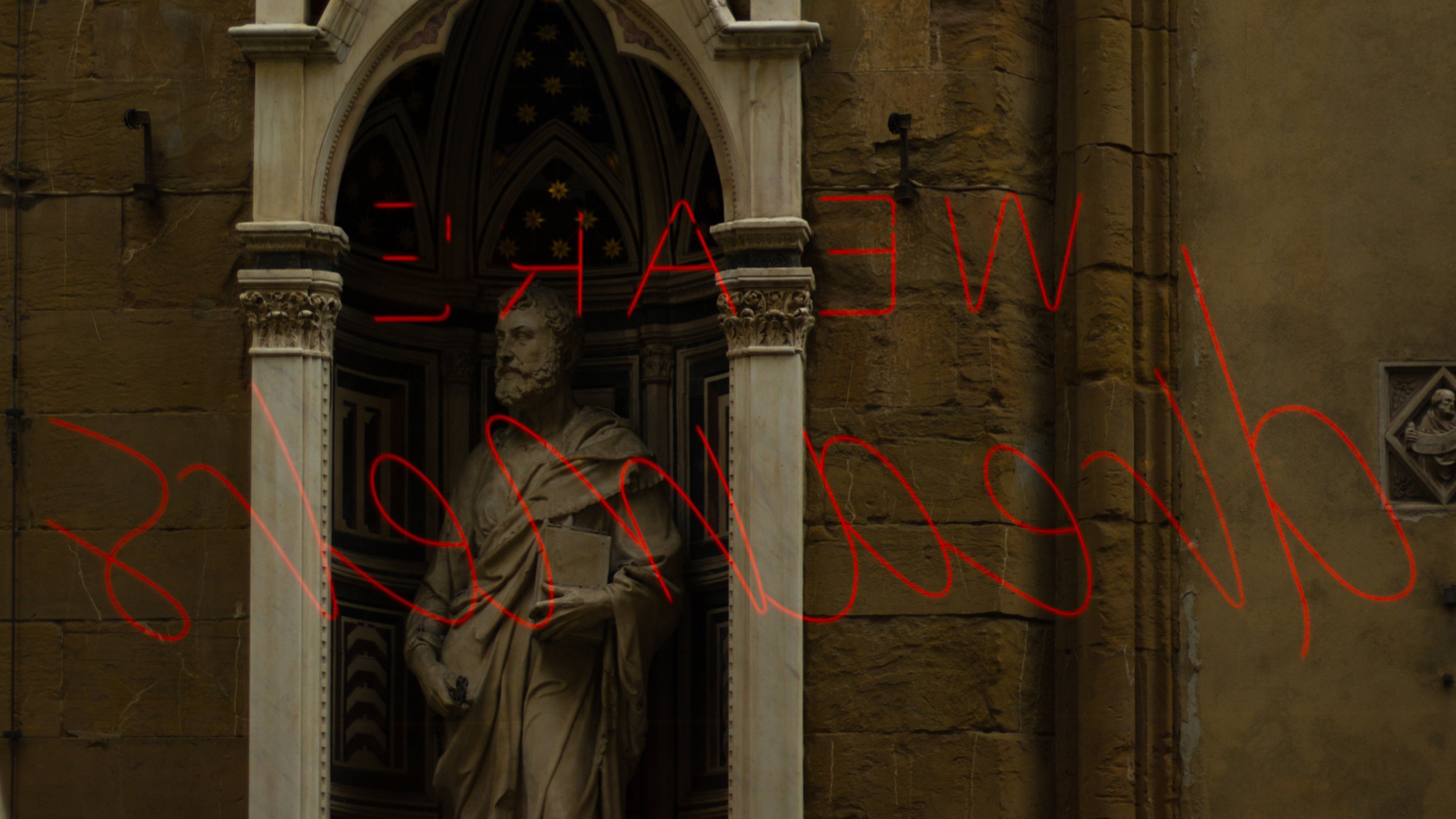 Statue of a man in a niche on a stone building, with architectural details and a decorative panel in the background, overlaid with red neon text.